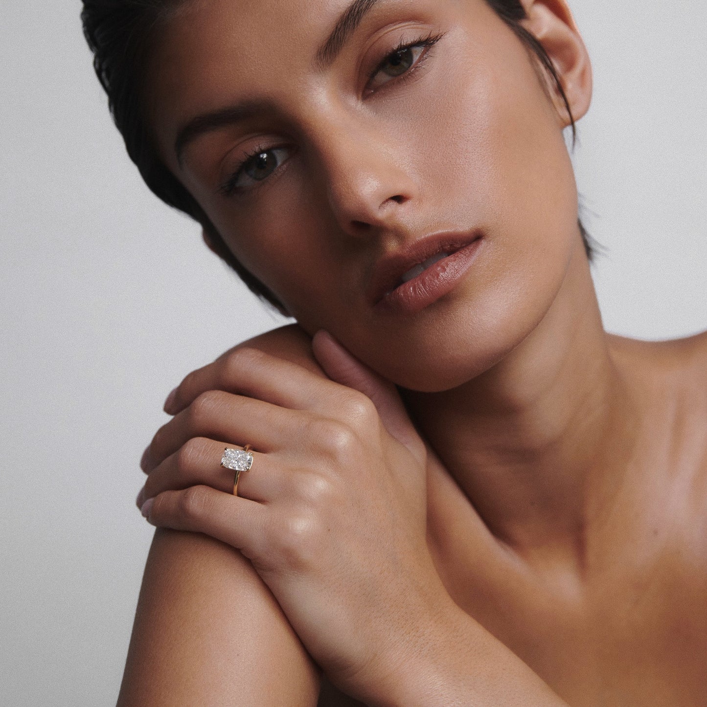 Woman with close-cropped dark hair wearing an elegant, large oval diamond ring on her finger. Minimalist style, luxury jewellery focus.