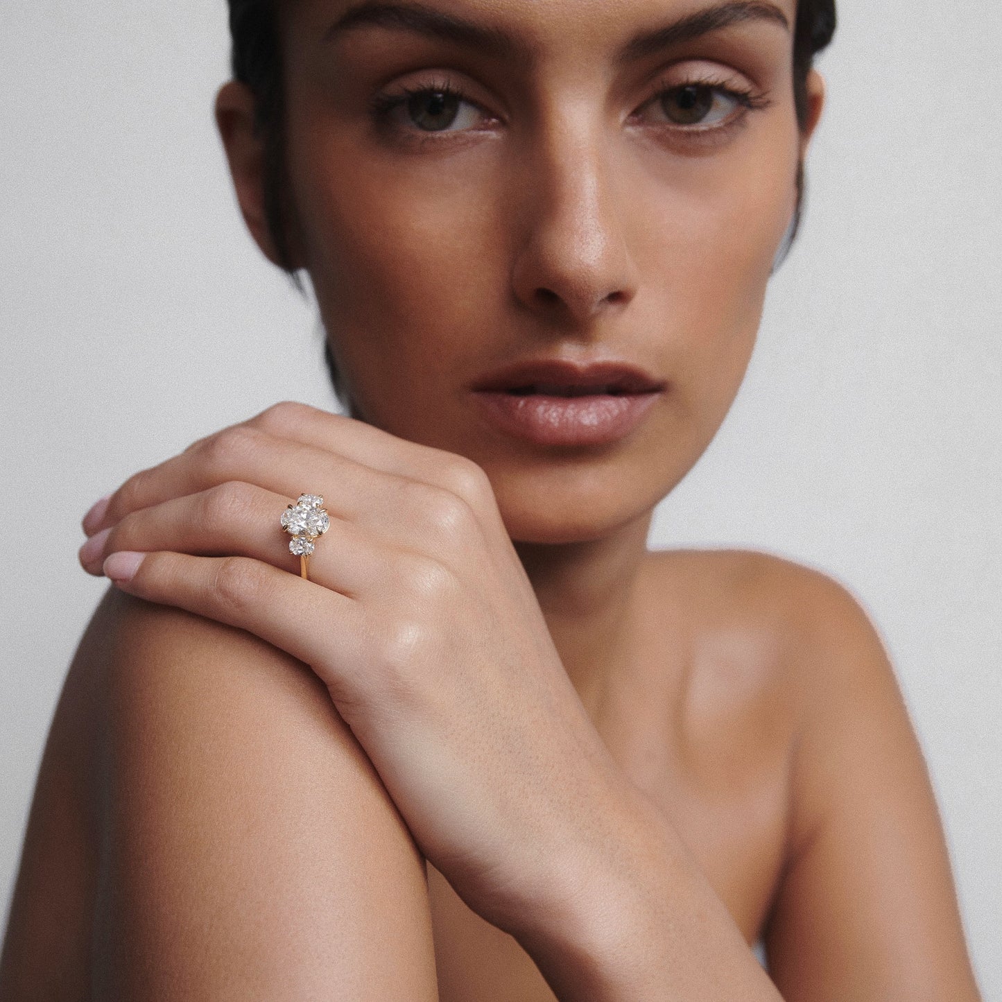 Woman showcasing a luxury diamond cluster ring on her finger, with a soft-focus background. Elegant high-end jewellery close-up.