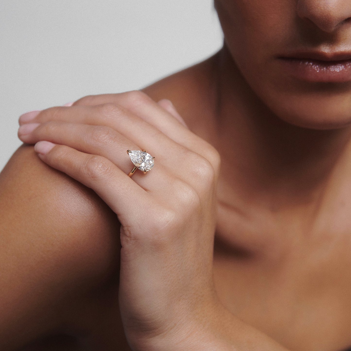 A person wearing a gold ring with a large pear-shaped diamond, showcasing luxury jewellery and elegance against a neutral background.