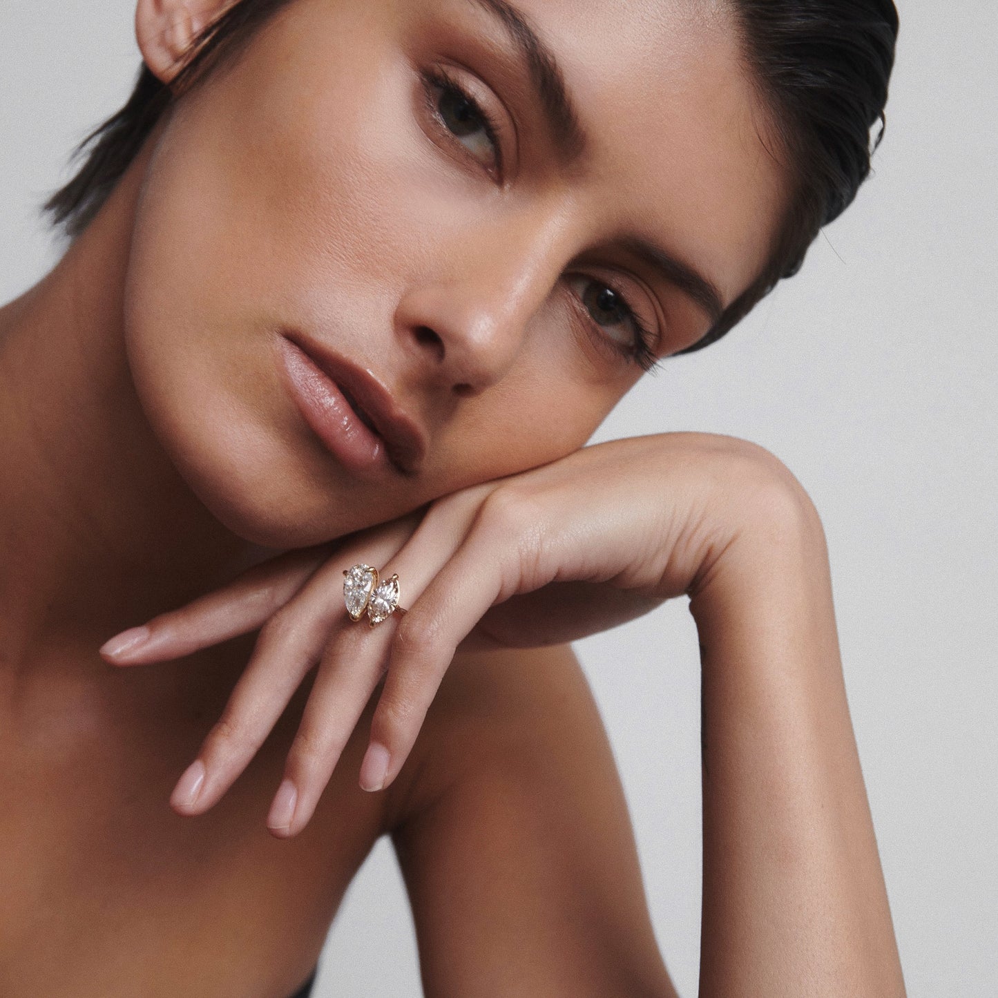 Woman wearing a luxurious diamond ring, rests her chin on her hand, showcasing elegant jewellery in a serene pose.