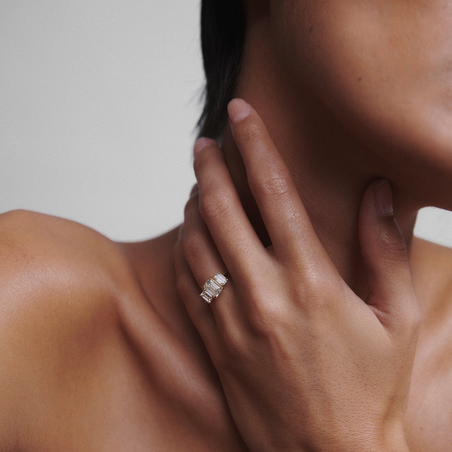 Close-up of a person’s hand adorned with elegant gold rings, featuring baguette-cut diamonds. The hand gently rests on their neck, showcasing luxury jewellery.