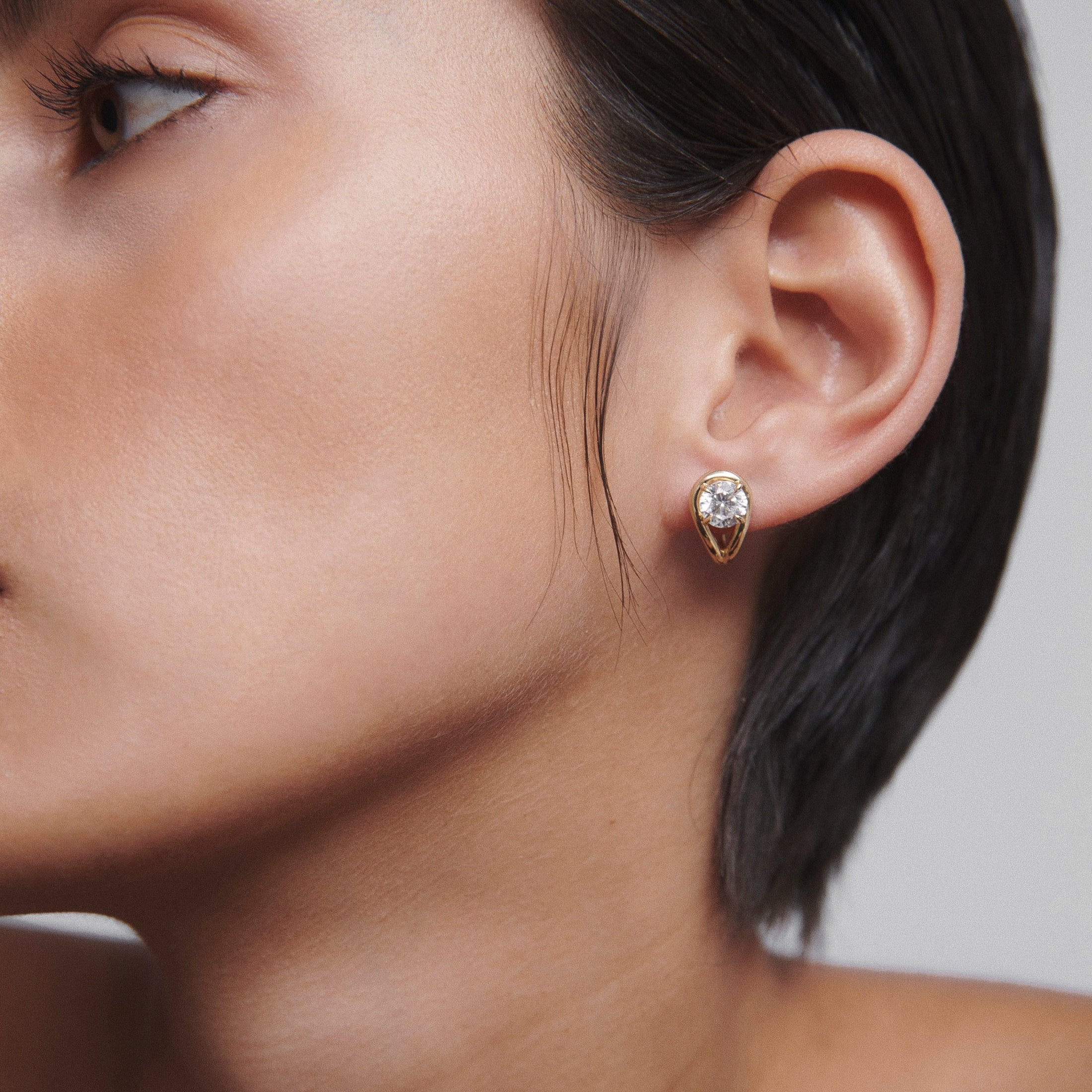 Close-up of a woman's ear wearing a gold and diamond teardrop earring, showcasing high-end jewellery elegance.