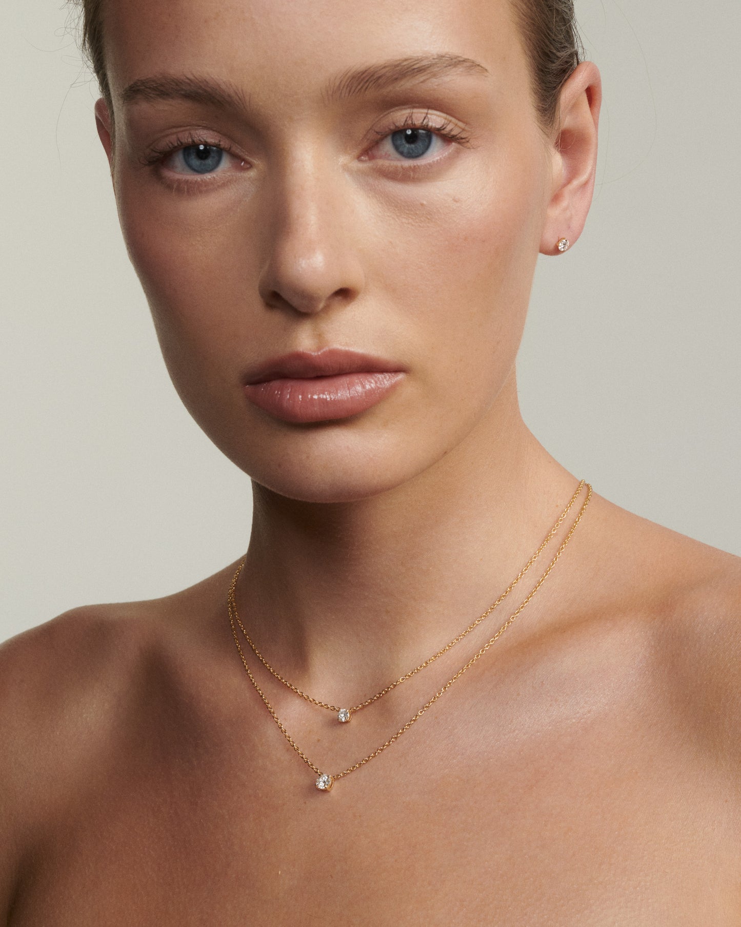 Close-up of a woman wearing a delicate gold necklace on a neutral background