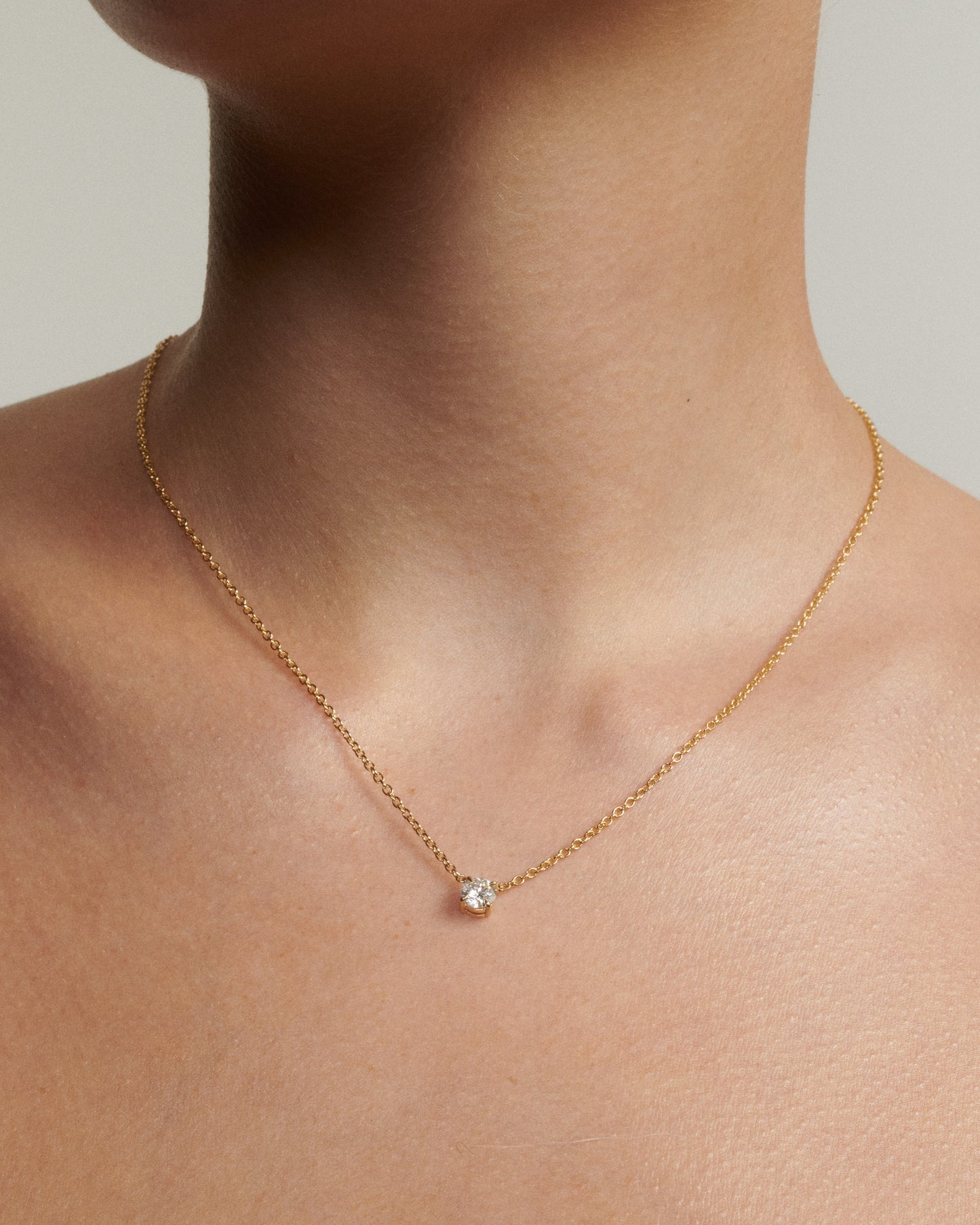 Gold necklace with a small gemstone on a person's neck against a neutral background