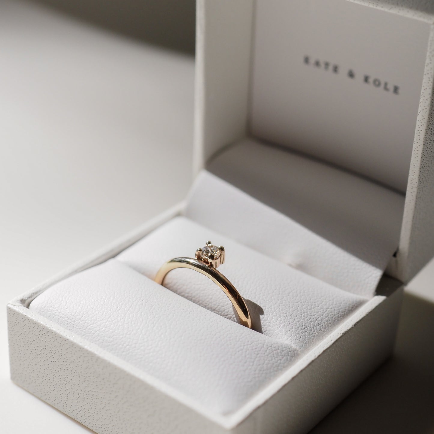 Gold solitaire engagement ring with a round diamond in a white box.