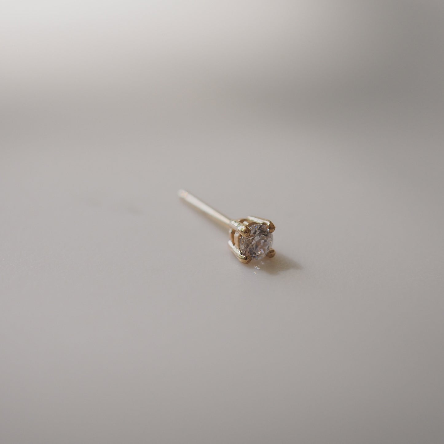 Single diamond stud earring set in gold on a smooth, light-coloured surface. Elegant, minimalist luxury jewellery.