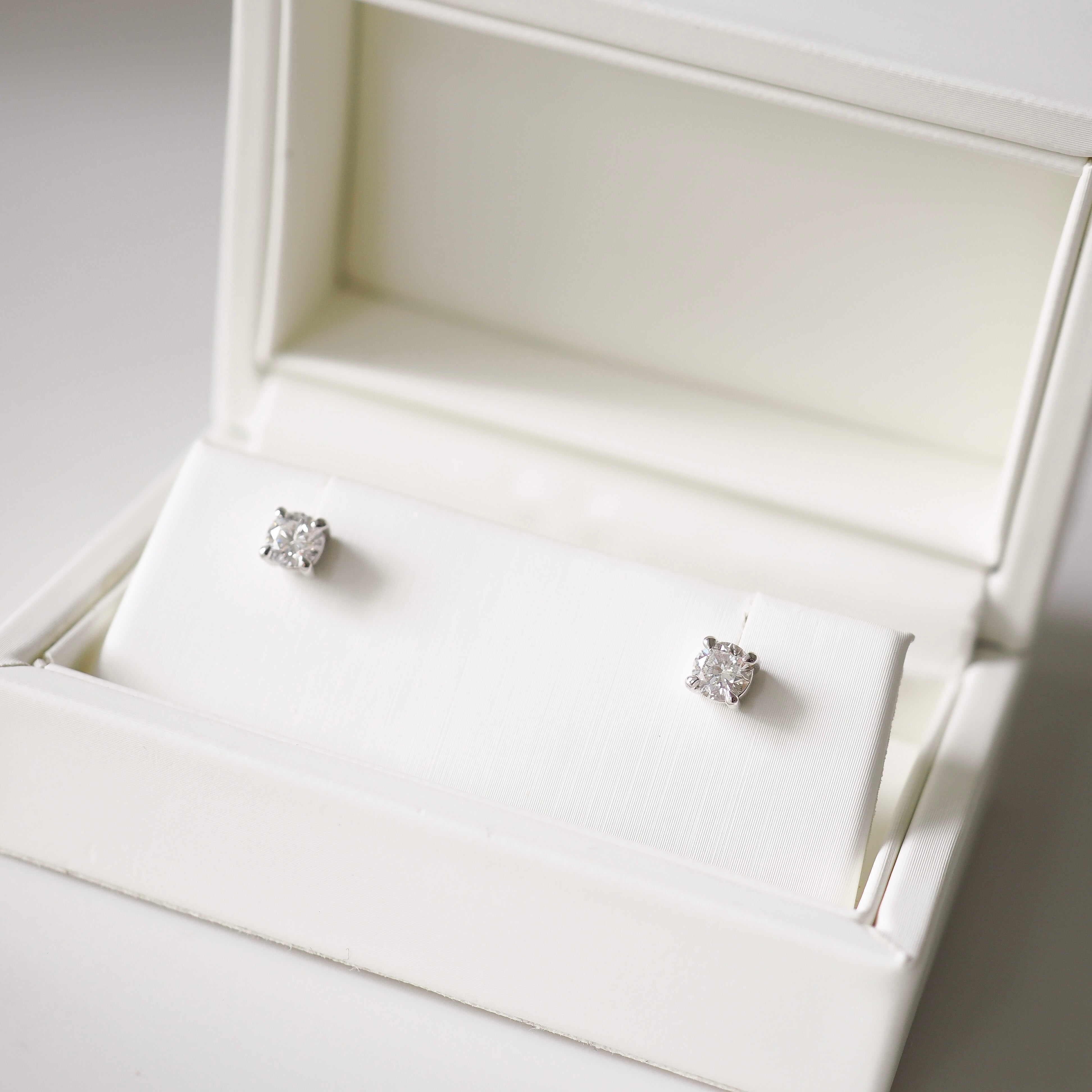 Pair of diamond stud earrings in an open white jewelry box.