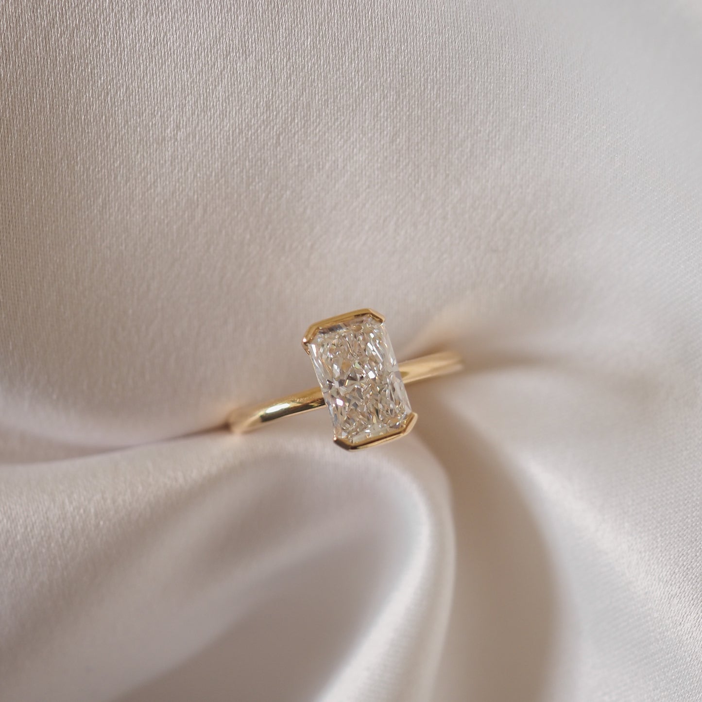 A radiant-cut diamond ring with a gold band, elegantly displayed on silky white fabric, showcasing luxury jewellery craftsmanship.