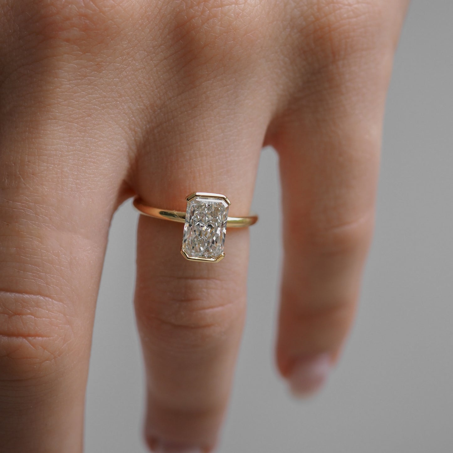 A hand wearing a gold ring with a large, rectangular diamond, showcasing elegant, minimalist luxury jewellery design.