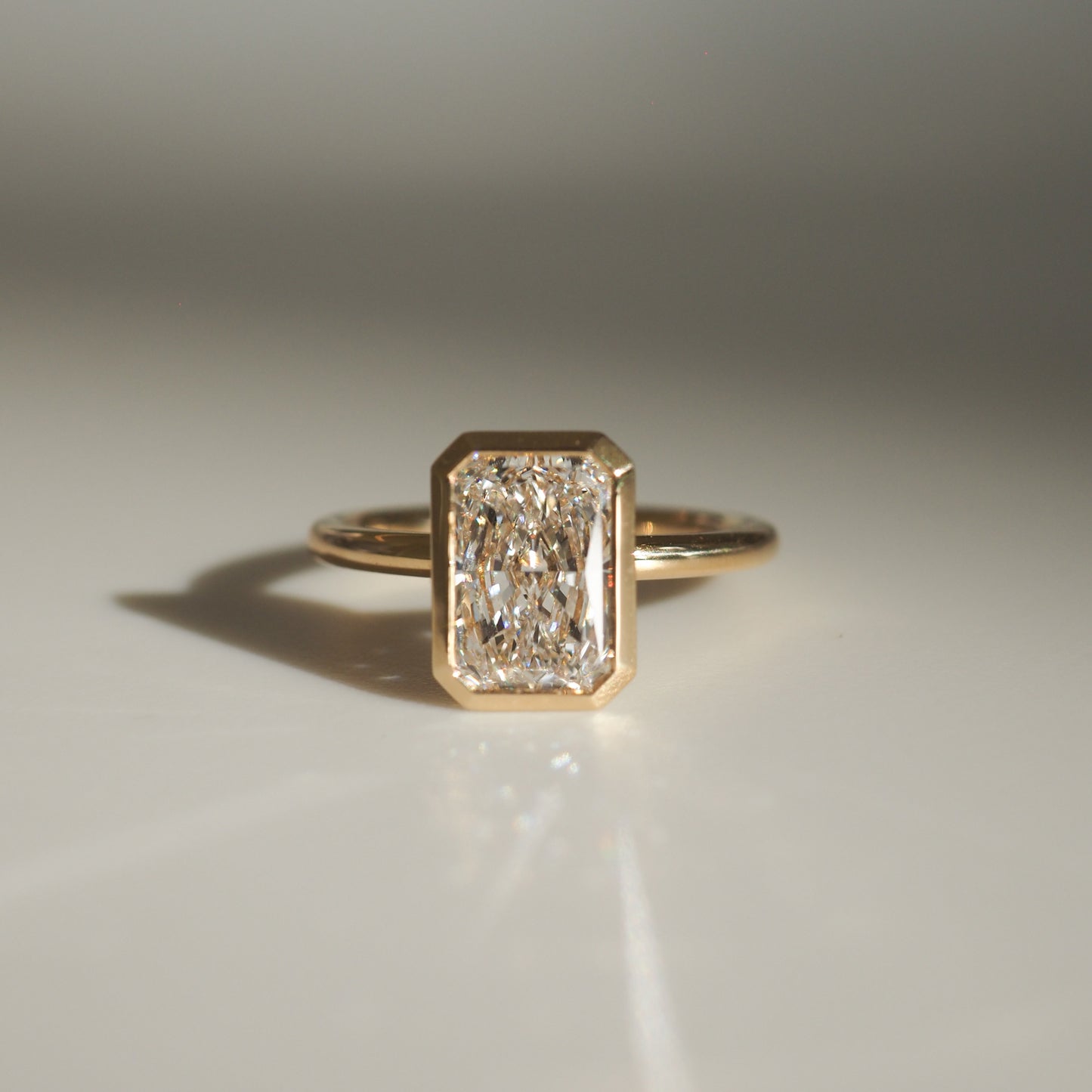 Elegant gold ring featuring a large emerald-cut diamond, reflecting light on a smooth, neutral surface. Luxurious jewellery design.