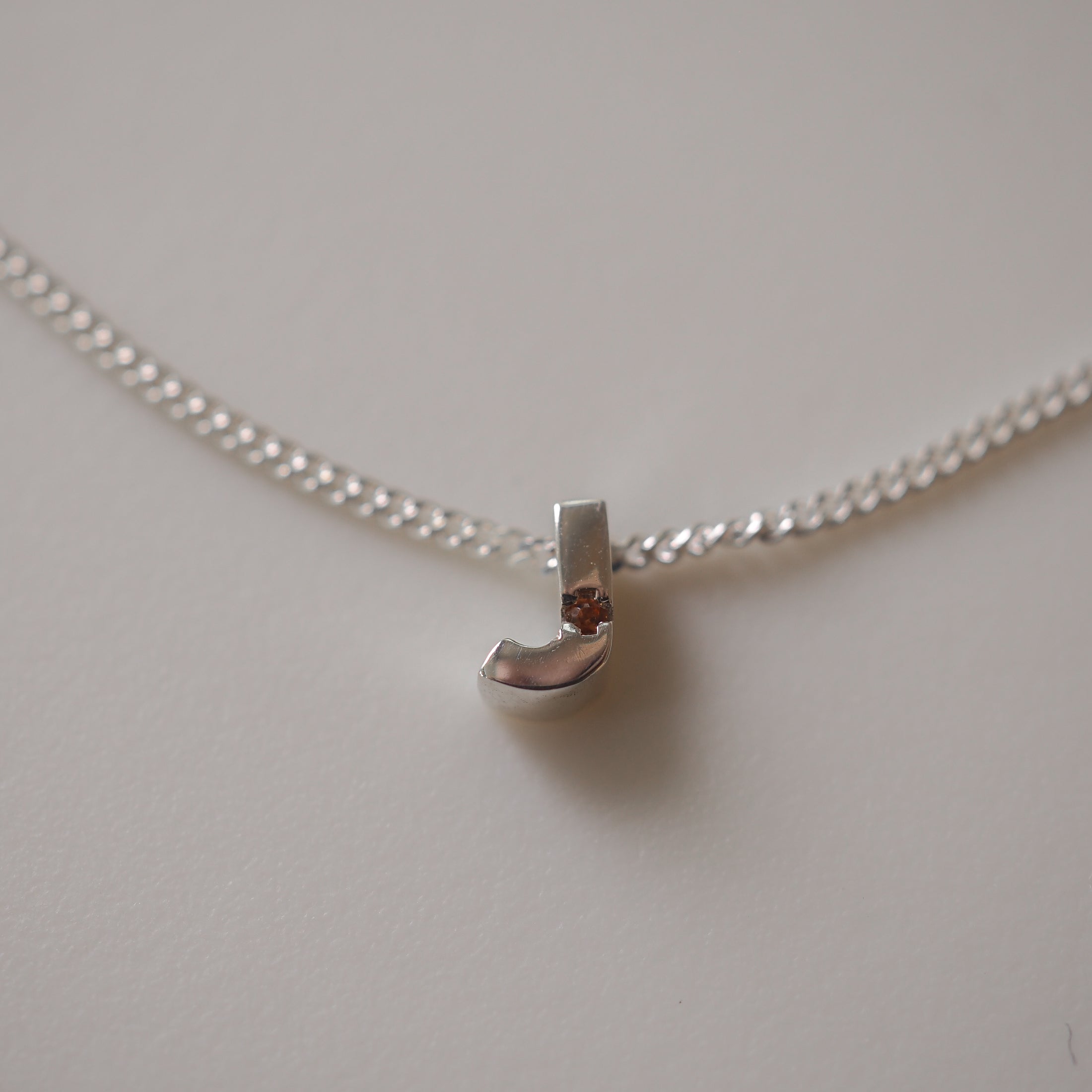 Silver chain necklace with a sleek 'J' pendant on a light background, showcasing minimalist luxury jewellery design.