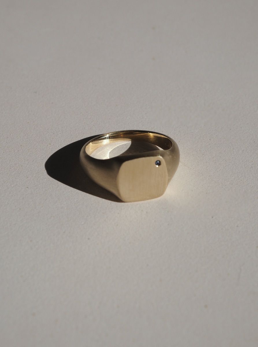 Elegant gold signet ring with a minimalist design, featuring a small central gemstone, casting a soft shadow on a light surface.
