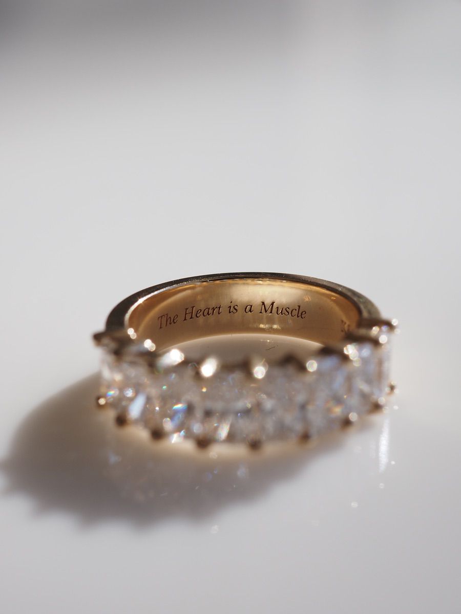 Gold band ring with sparkling clear gemstones, inscribed inside with "The Heart is a Muscle". Luxury jewellery, elegant design.