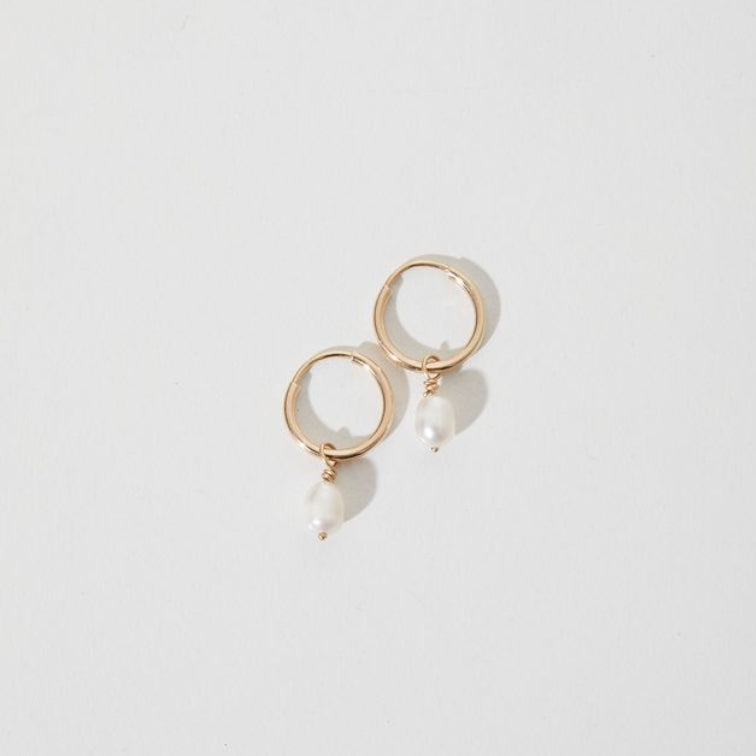 Pair of gold hoop earrings with dangling white pearls on a minimalist white background. Ideal for luxe fashion and jewellery styles.