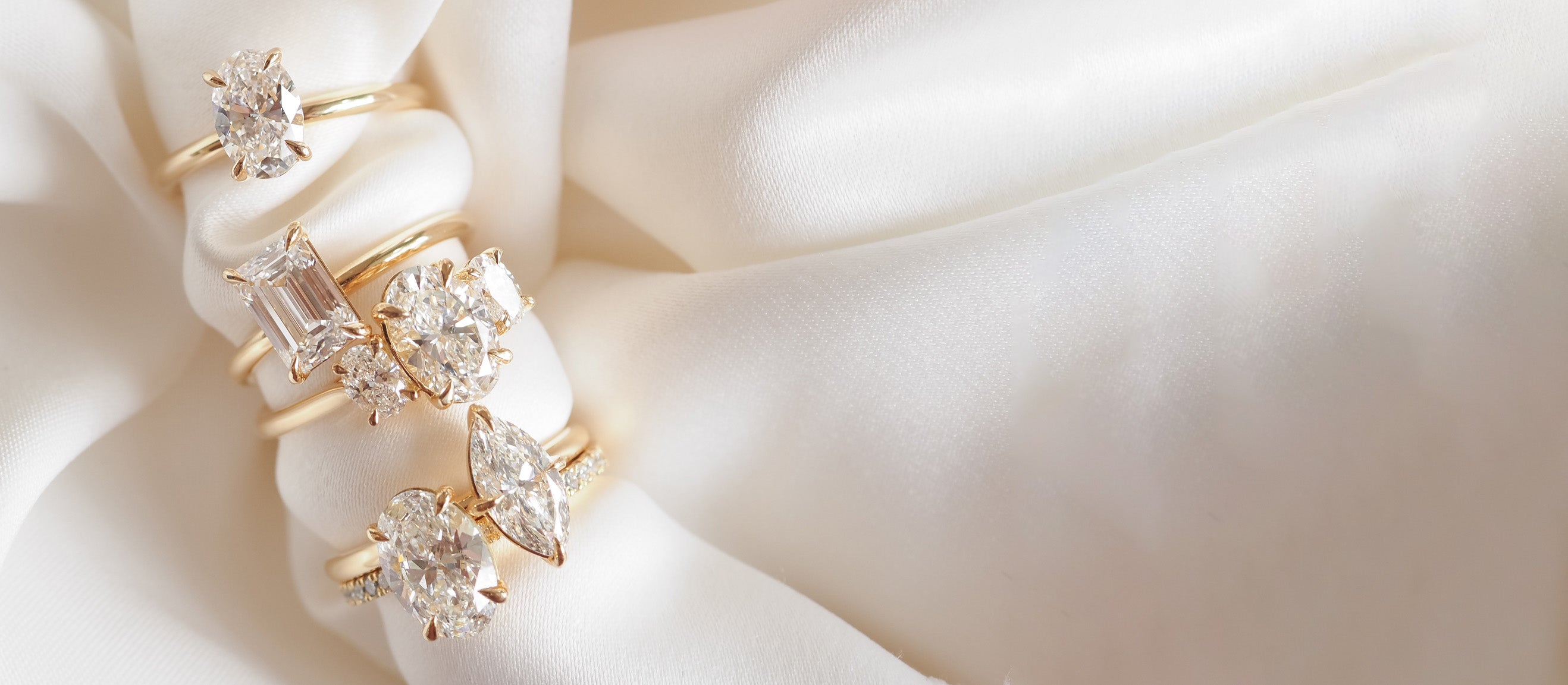 Close-up of elegant diamond rings with various cuts on a silky white fabric, highlighting luxury and craftsmanship in fine jewellery.