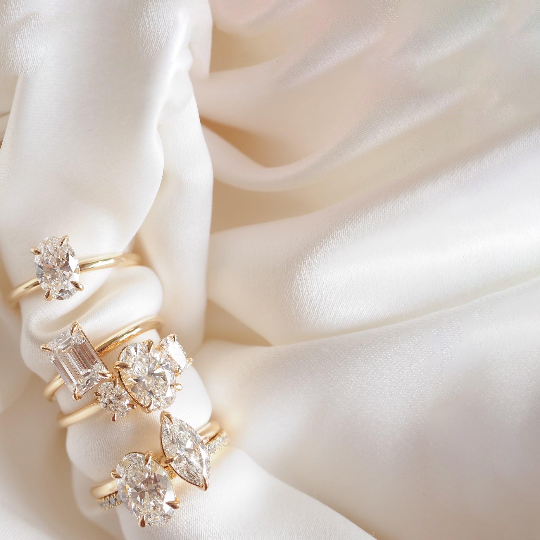 Elegant gold rings with various diamond cuts on flowing white silk, showcasing luxury jewellery design and craftsmanship.