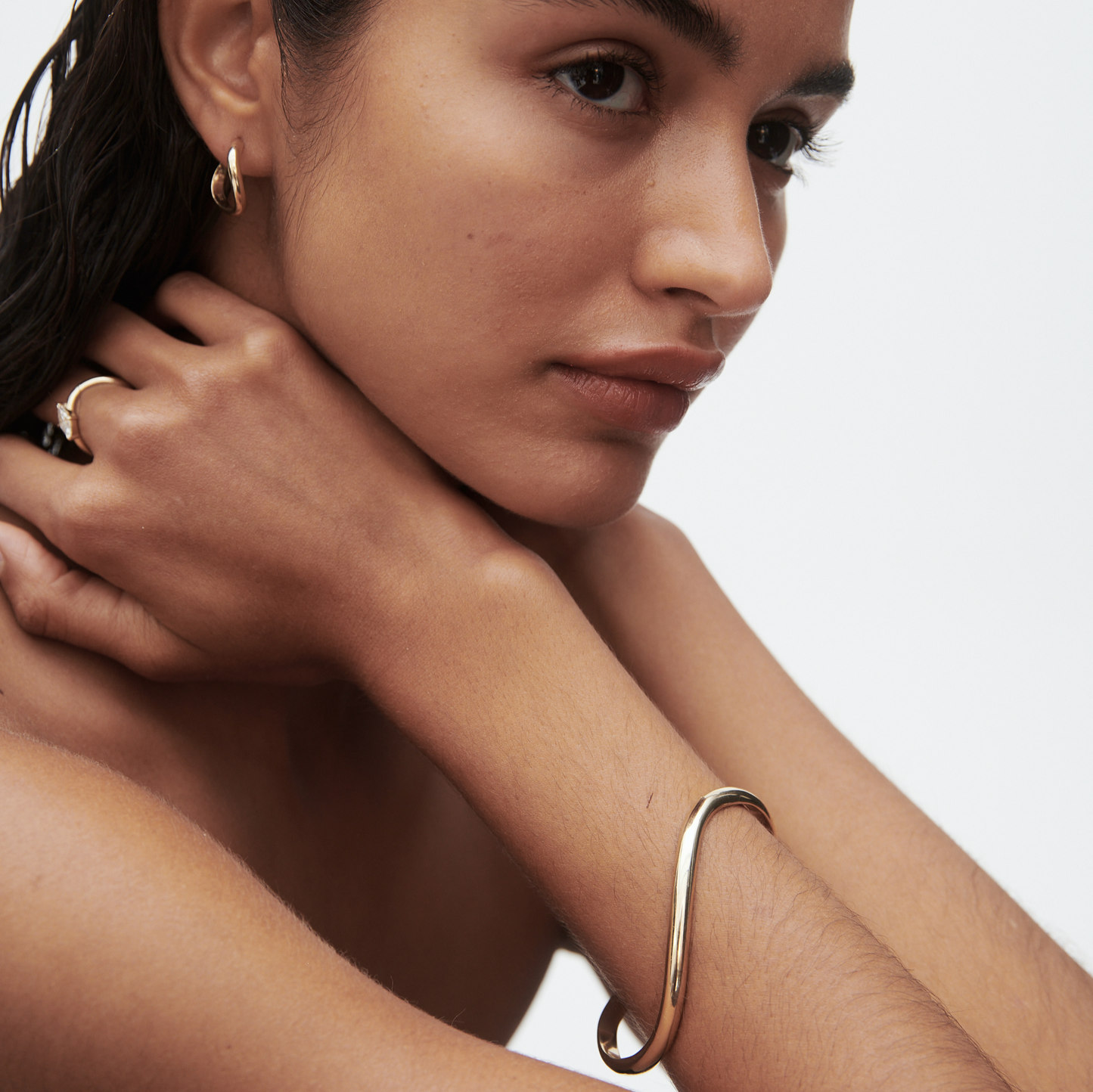 Model wearing luxury gold hoop earrings, a sleek gold bracelet, and a matching ring, showcasing elegant high-end jewellery.