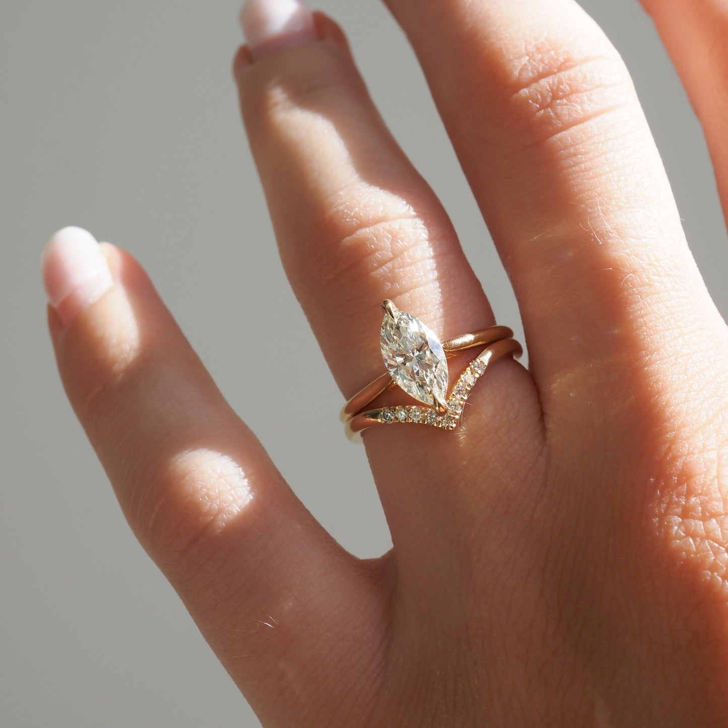 Hand displaying a marquise-cut diamond engagement ring with a gold band, paired with a diamond-studded V-shaped ring in natural light.