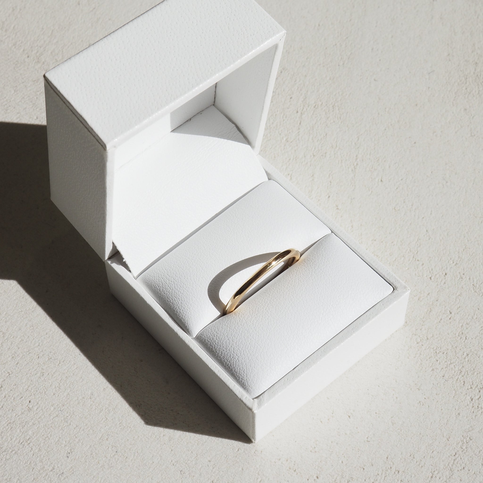 Elegant gold ring in a white jewellery box, casting a shadow. Perfect for luxury or engagement jewellery presentations.