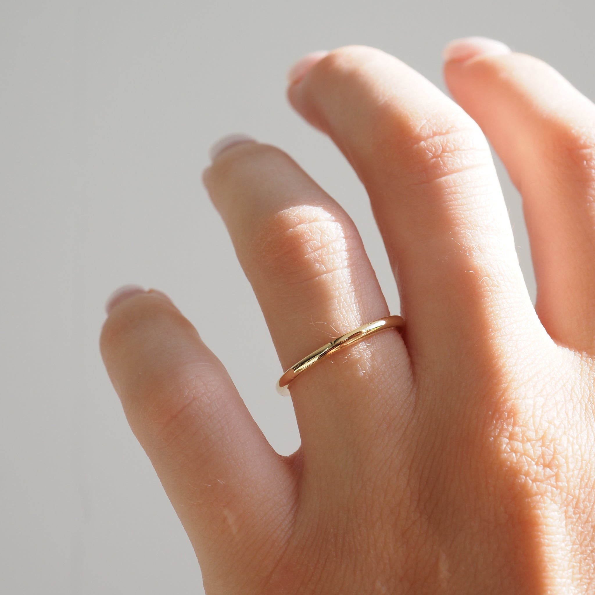 Hand with a simple gold band on a finger, set against a neutral background. Perfect for minimalist jewellery lovers.