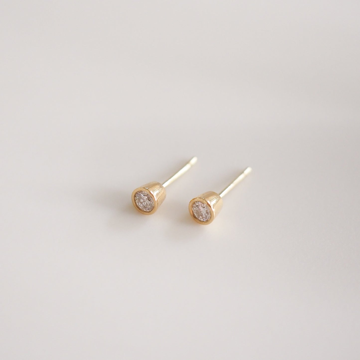 Gold stud earrings with round diamonds, displayed on a soft white background. Elegant and minimalist design, luxury jewellery.