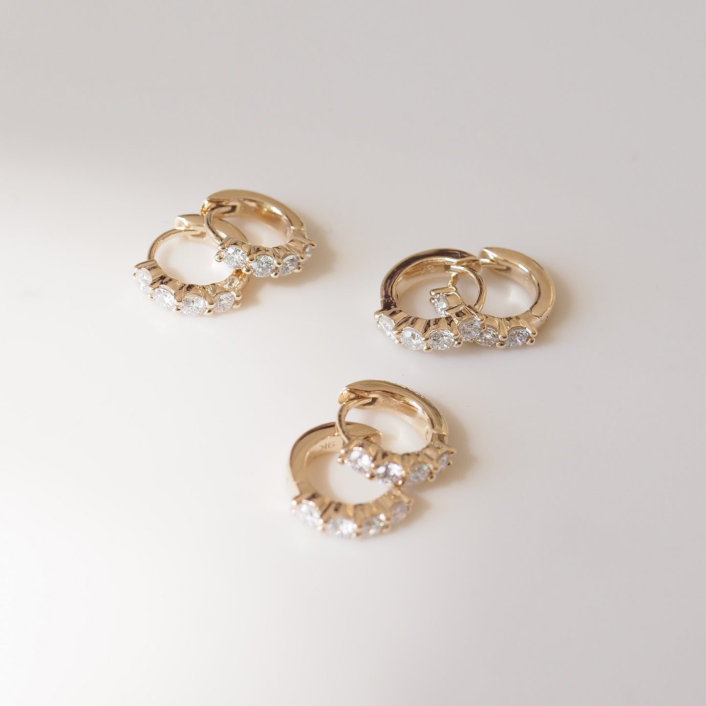 Three gold hoop earrings with clear gemstones on a light gray background