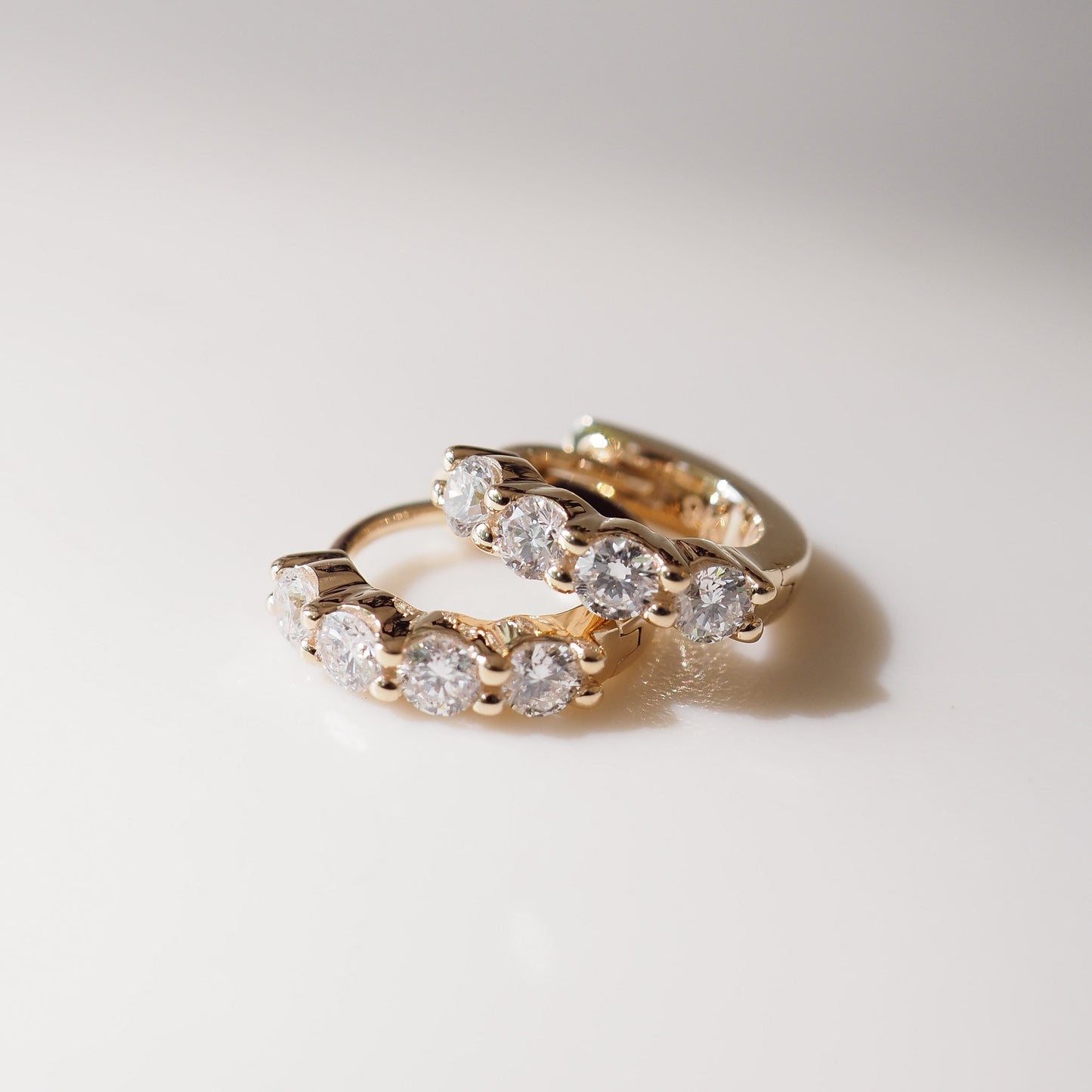 Pair of gold hoop earrings with clear gemstones on a light gray background