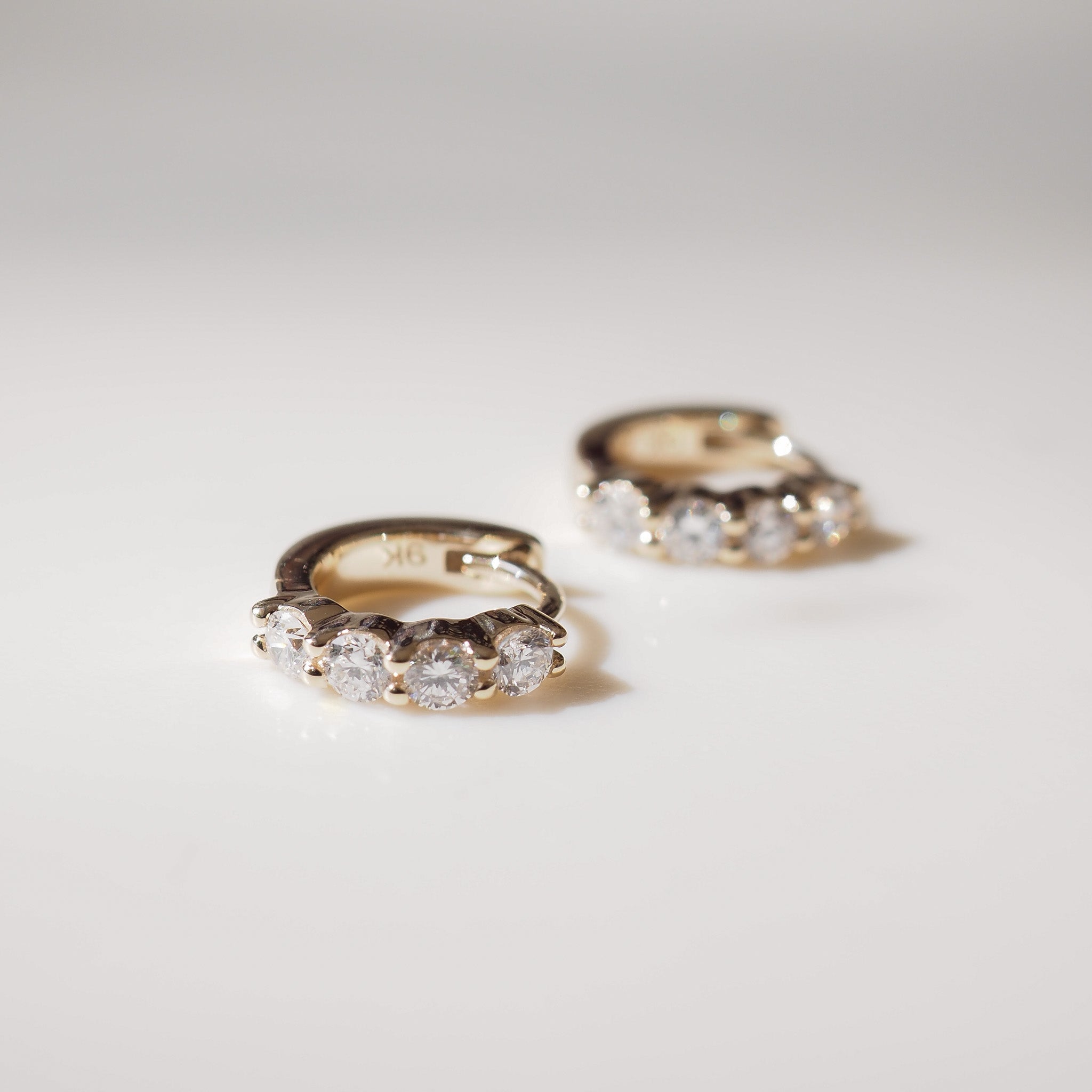 Pair of gold hoop earrings with clear gemstones on a light gray background