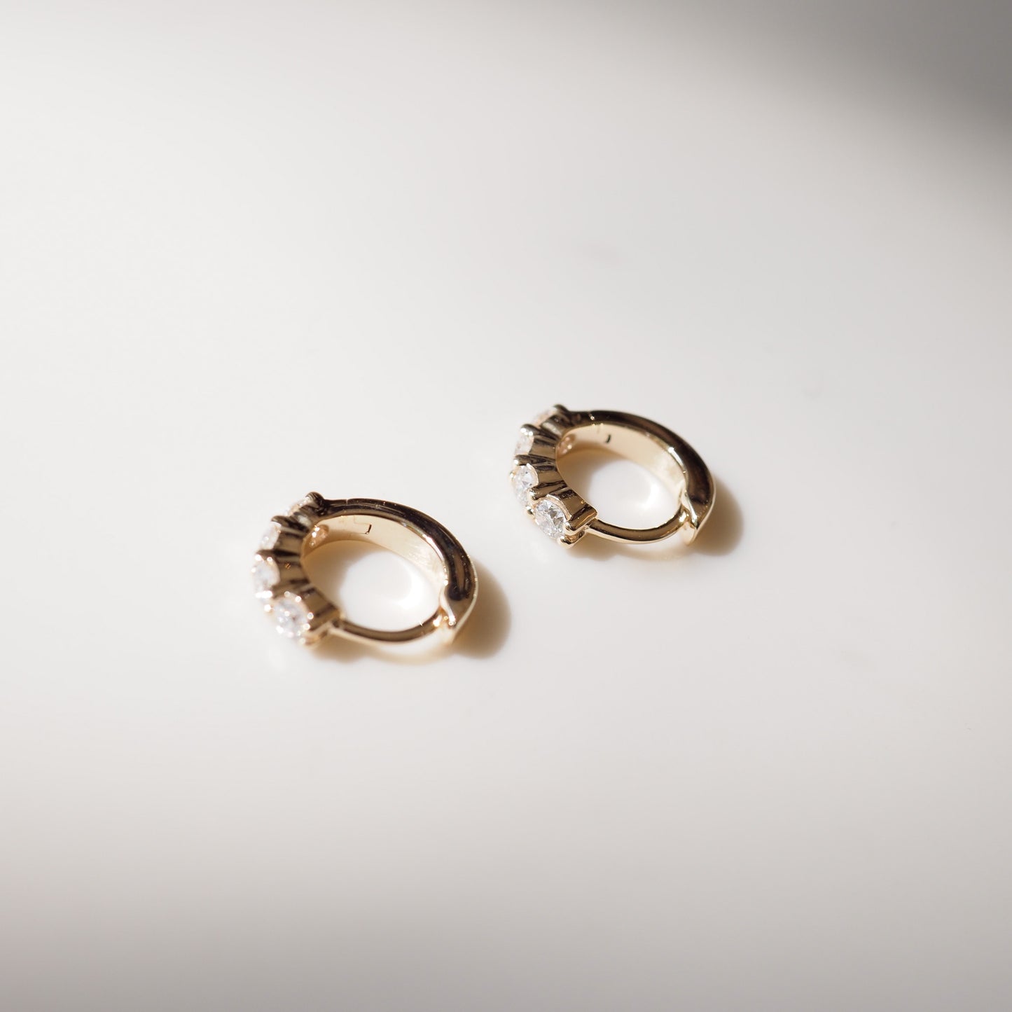 Gold hoop earrings with small stones on a light gray background