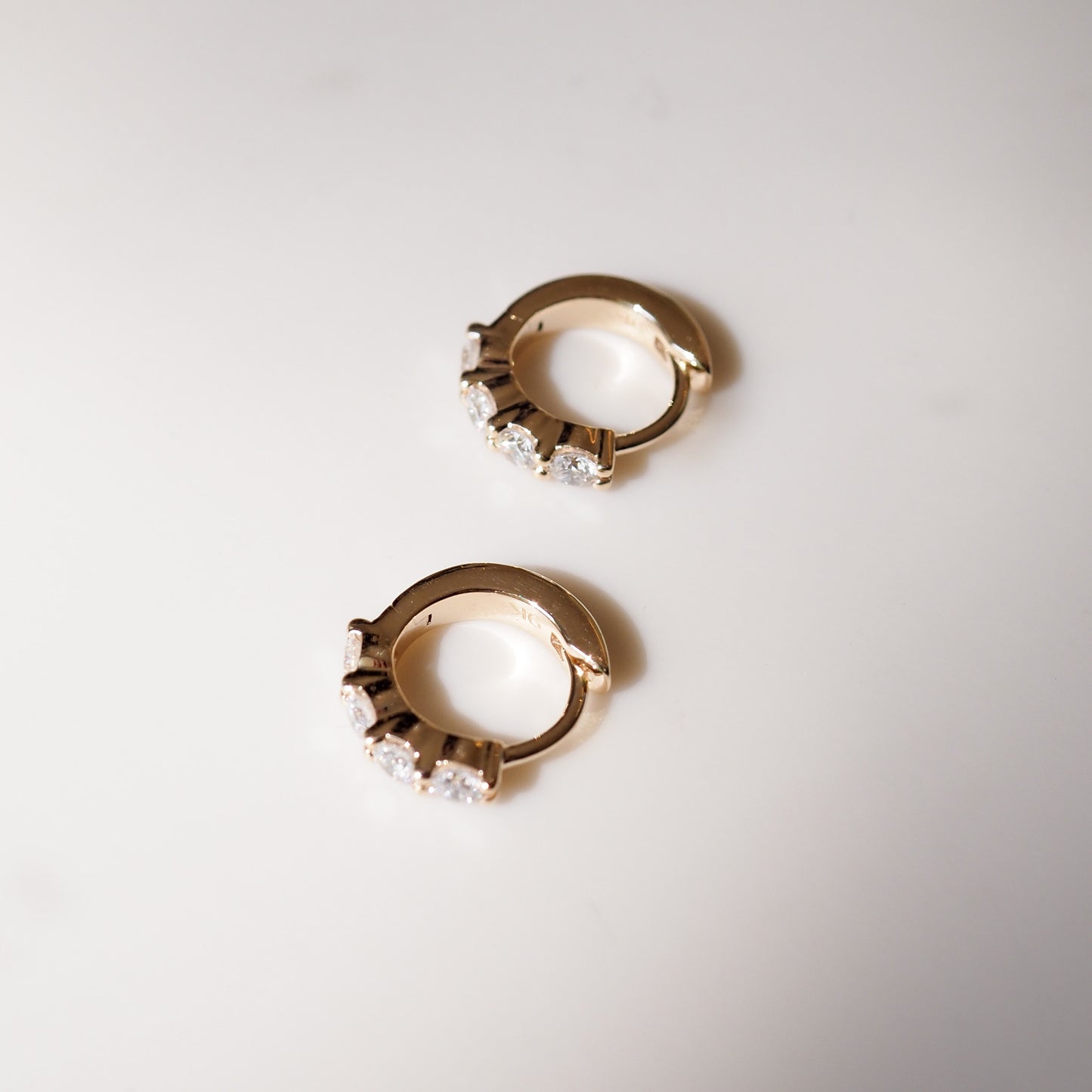 Pair of gold hoop earrings with clear gemstones on a light gray background