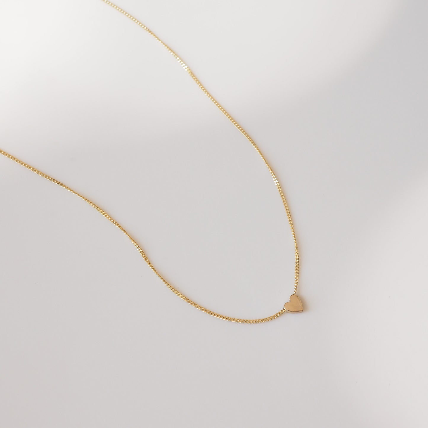 Gold necklace with a small heart pendant on a light gray background