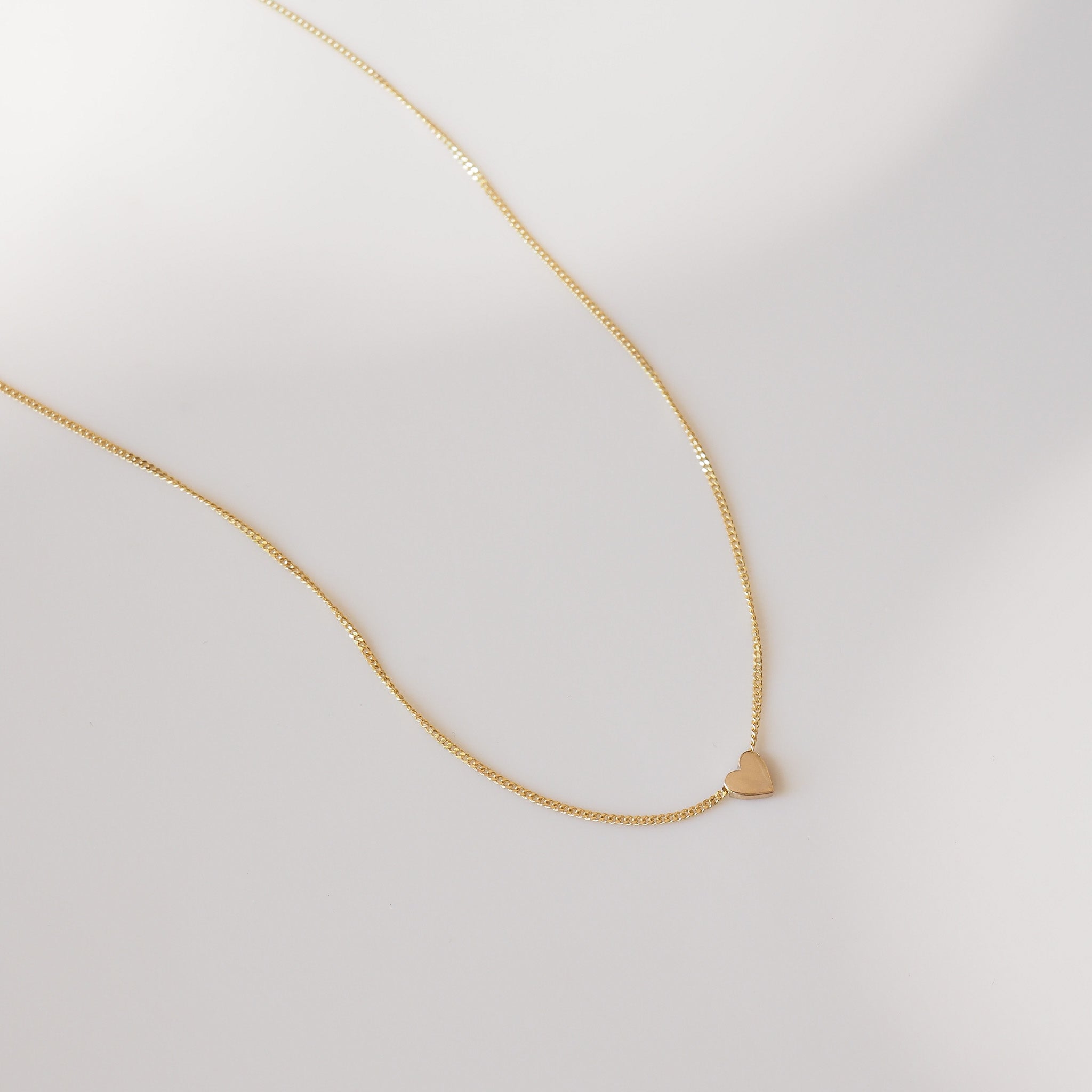 Gold necklace with a small heart pendant on a light gray background