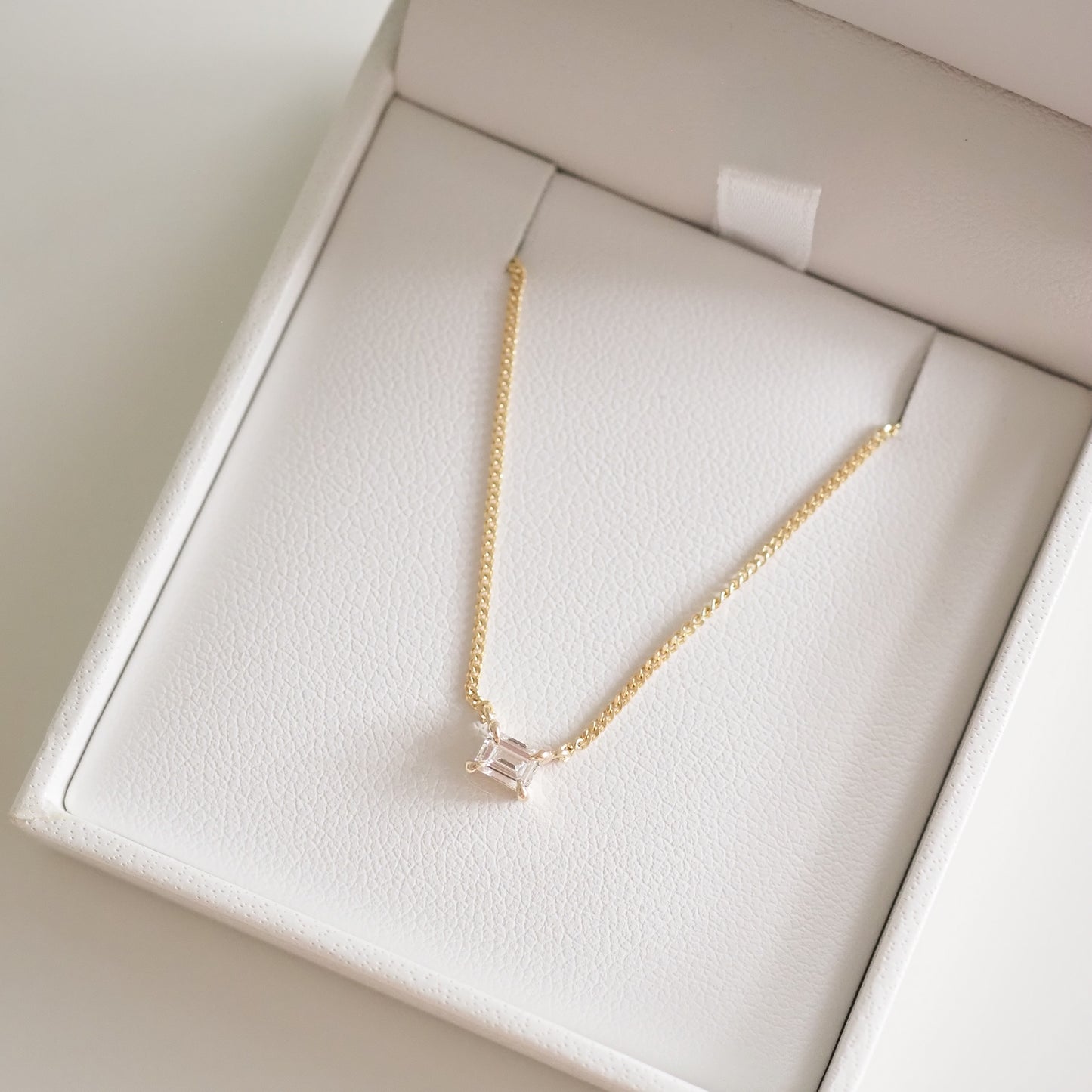 Gold necklace with a solitaire diamond pendant in a white jewellery box. Luxurious and elegant design, perfect for sophisticated style.
