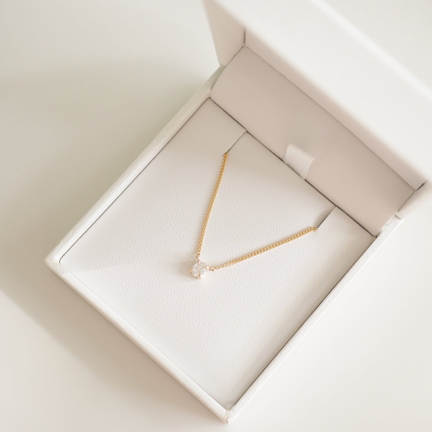 Gold chain necklace with diamond pendant in a white jewellery box, symbolising luxury and elegance.