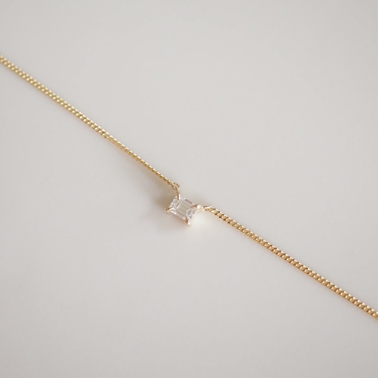 Elegant gold chain bracelet featuring a single emerald-cut diamond, showcased on a minimalist white background. Perfect for luxury jewellery lovers.