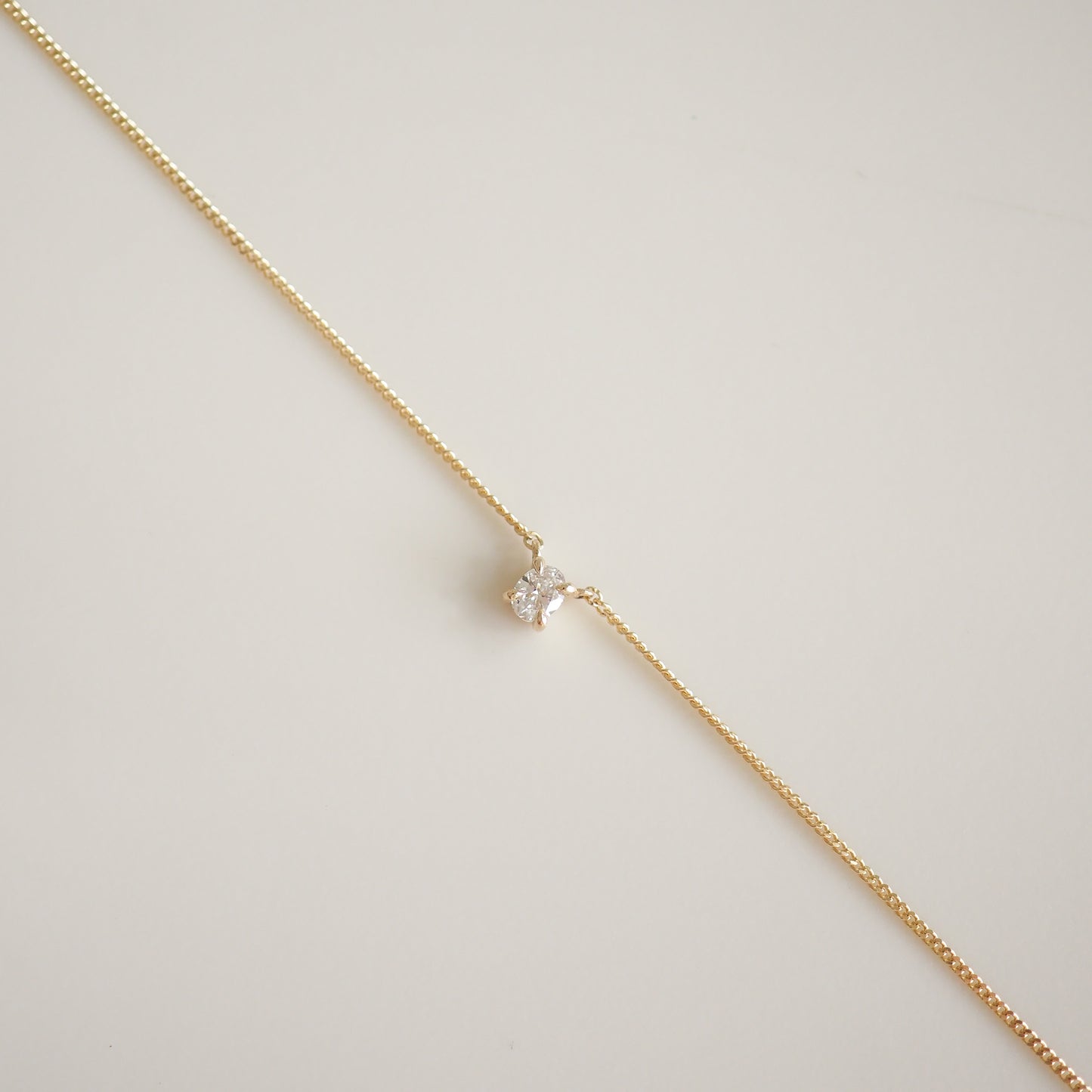 Delicate gold chain with a central sparkling diamond pendant on a light background. Sophisticated luxury jewellery design.