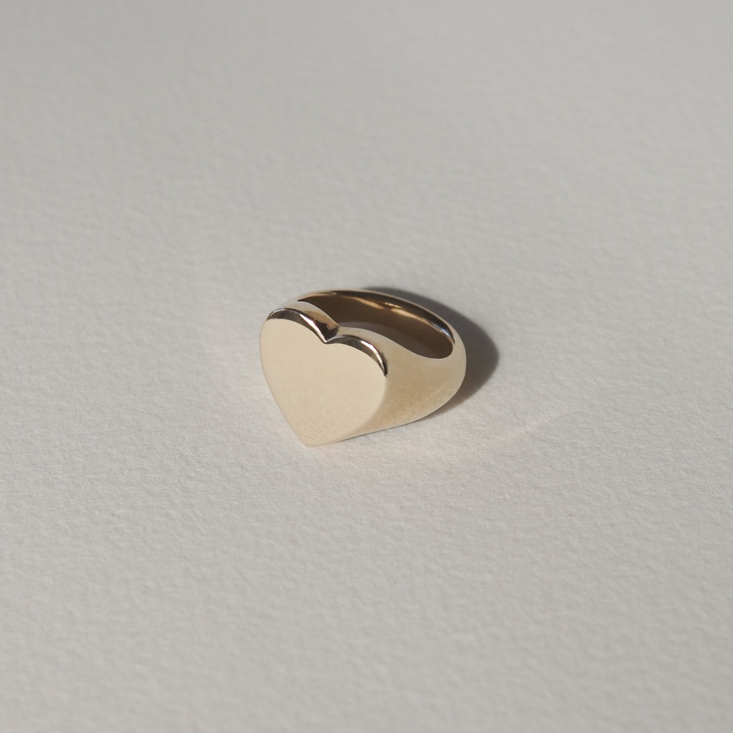 Gold heart-shaped ring on a light textured background, showcasing minimalist luxury jewellery design.