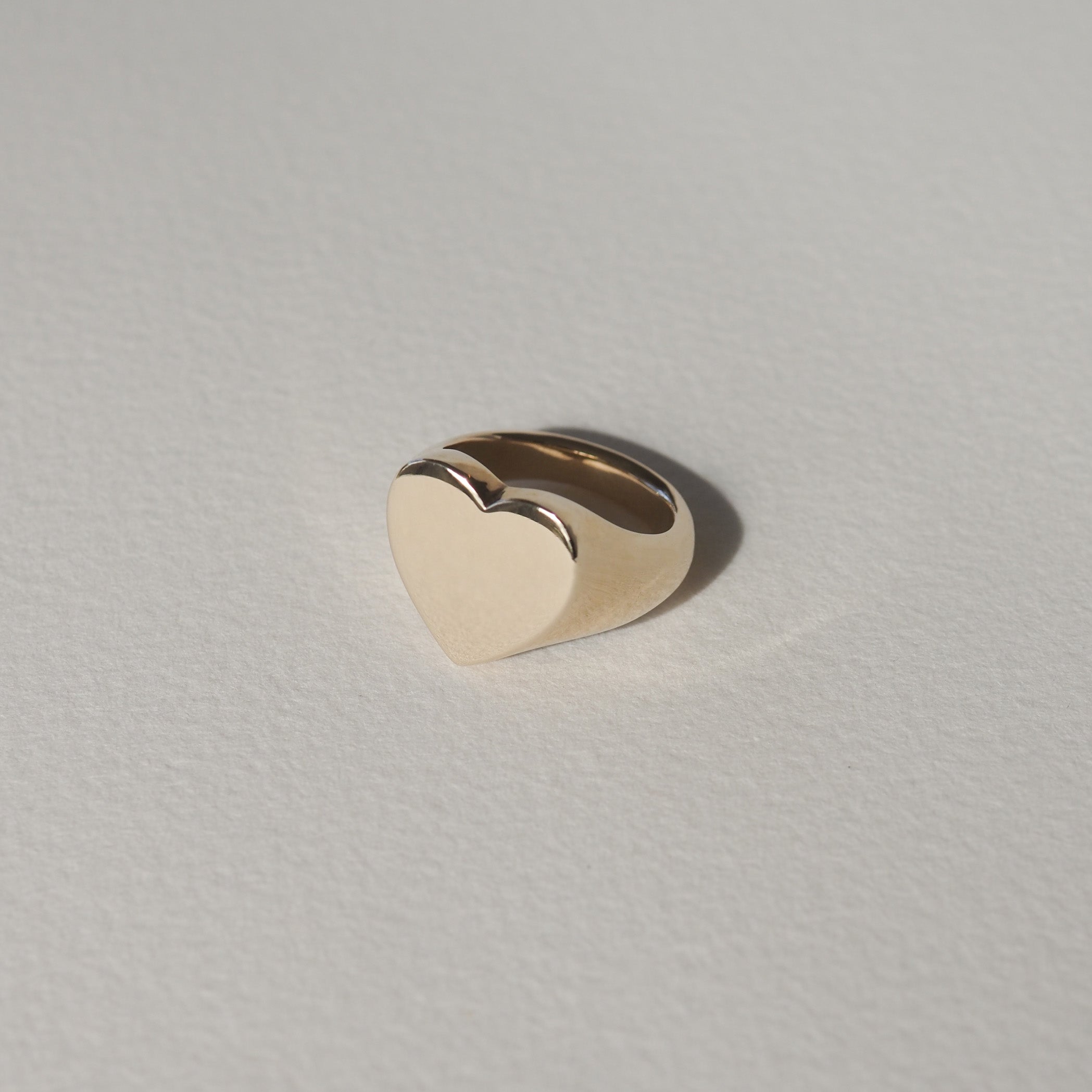Gold heart-shaped ring on a light textured background, showcasing minimalist luxury jewellery design.