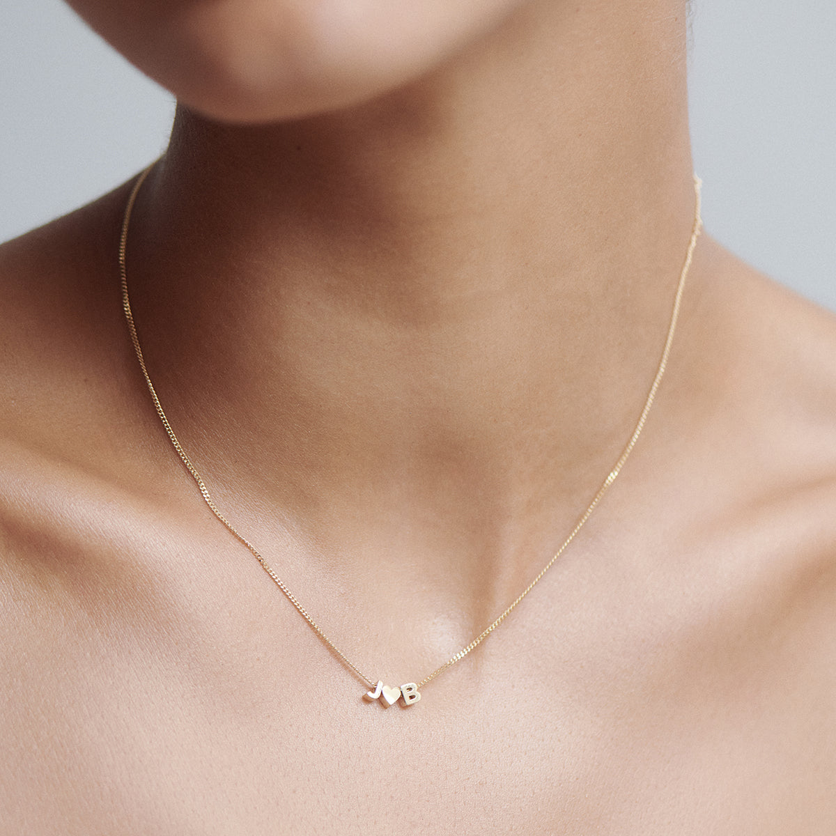 Elegant gold necklace with "J" and "B" initials on skin. Minimalistic and luxurious design. Perfect for personalised jewellery lovers.