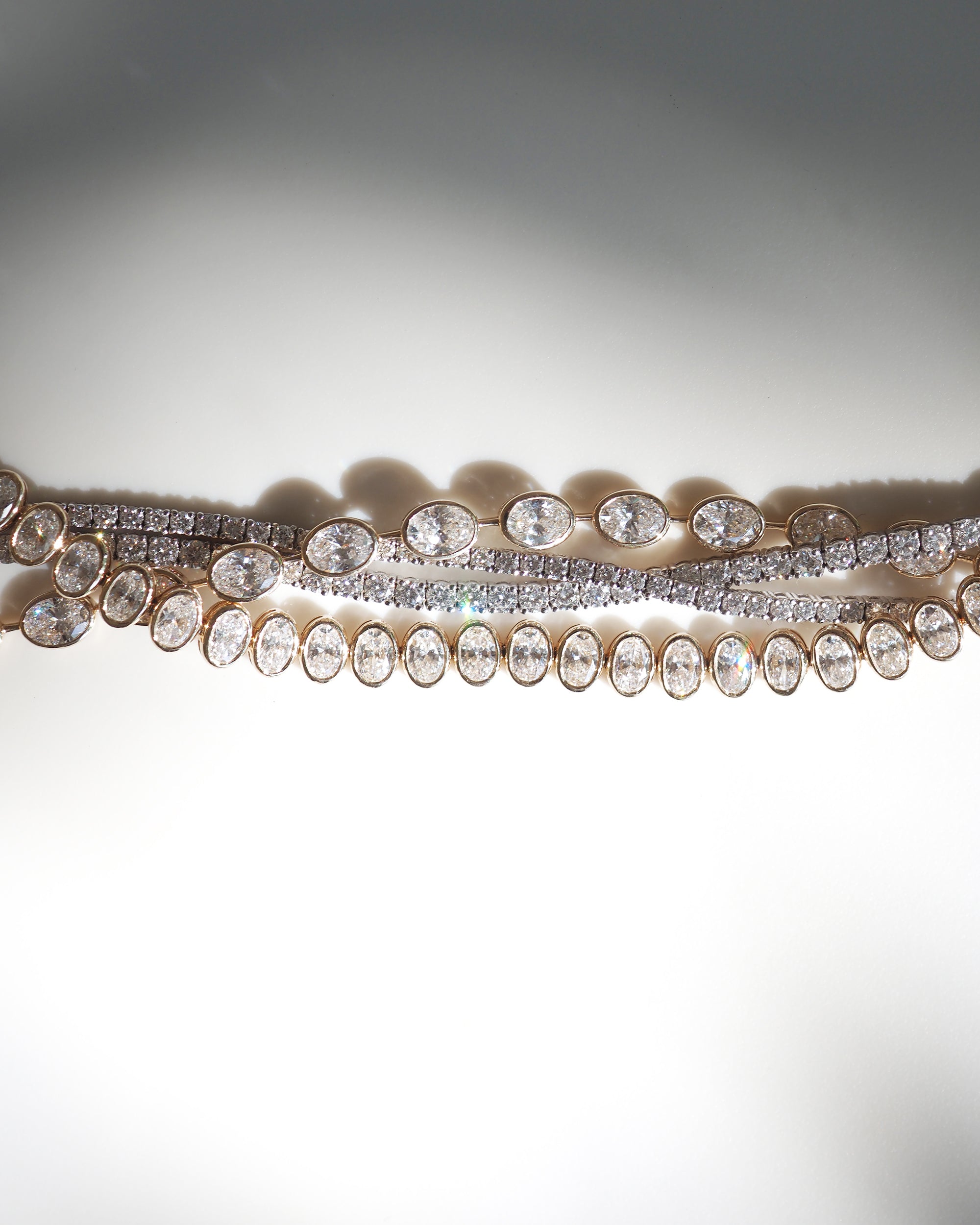 Three luxury diamond necklaces with oval and round stones, elegantly displayed on a soft, illuminated background. Perfect for high-end fashion.