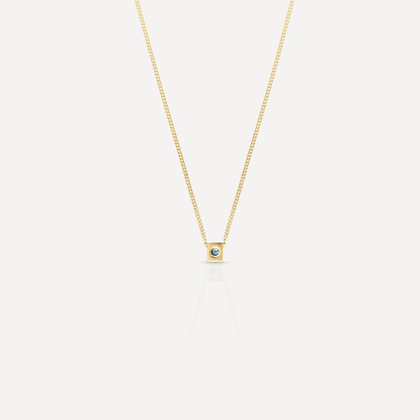 Gold necklace featuring a minimalist square pendant with a small blue gemstone, set against a light background. Luxury jewellery design.