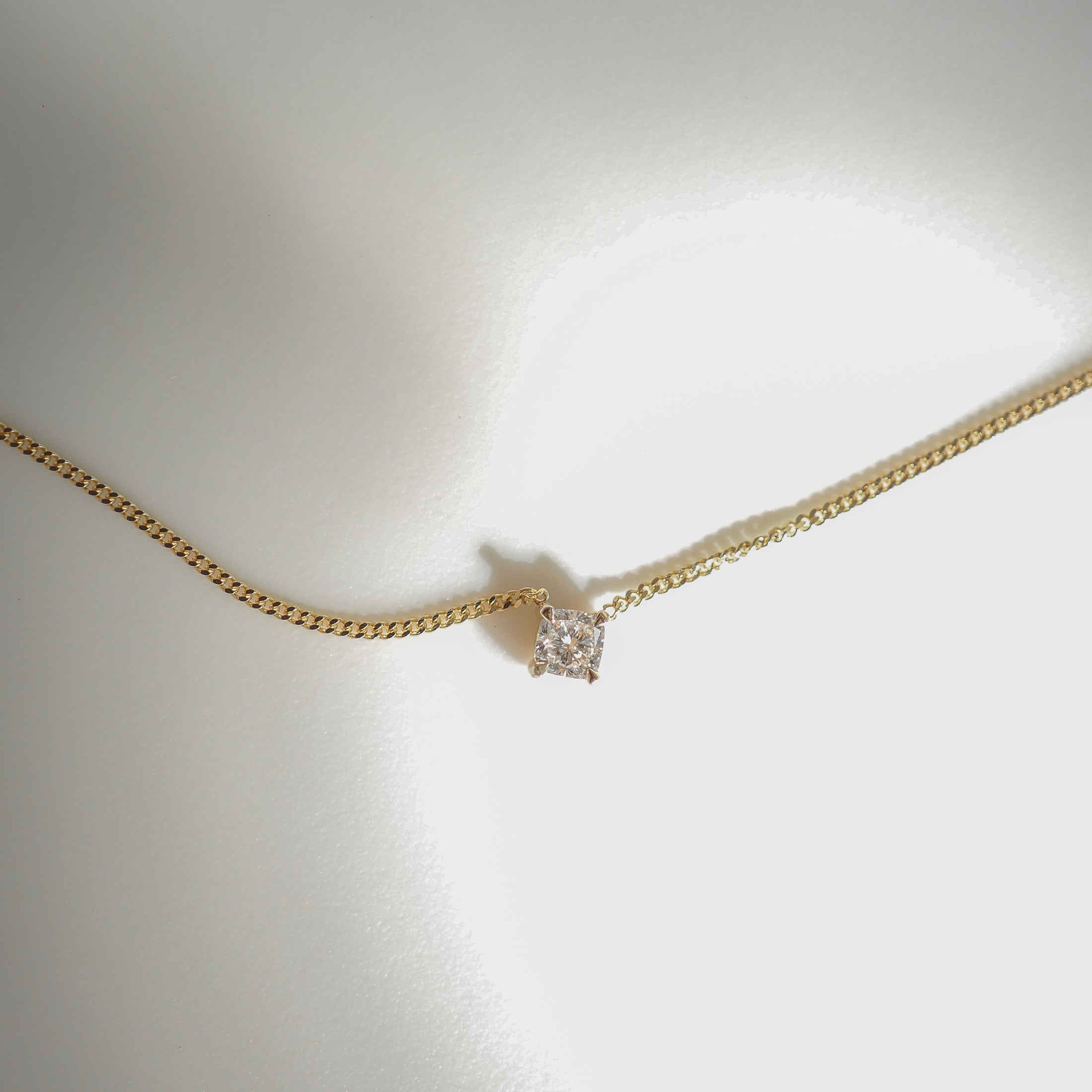 Gold chain necklace with a single square-cut diamond pendant on a light background, highlighting luxury jewellery design.