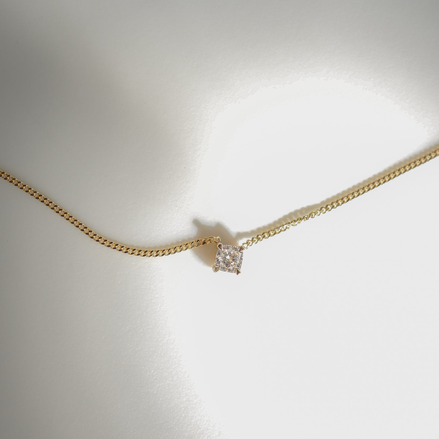 Elegant gold chain necklace with a solitaire diamond pendant on a soft grey background, highlighting luxury jewellery design.