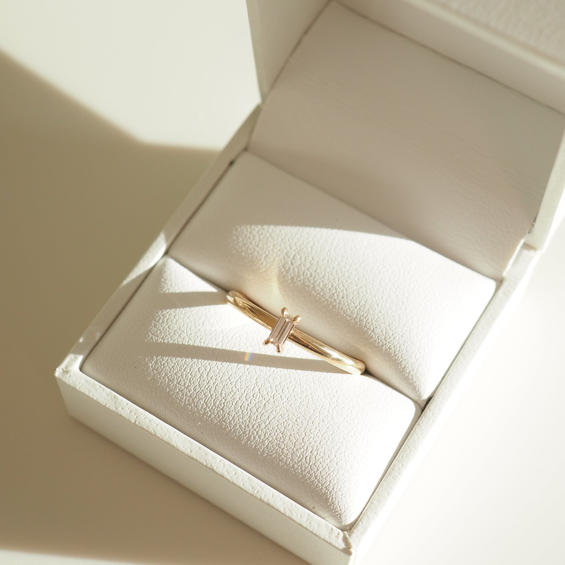 Gold ring with a baguette-cut diamond in a white jewellery box with soft lighting. Luxurious, elegant Australian jewellery piece.