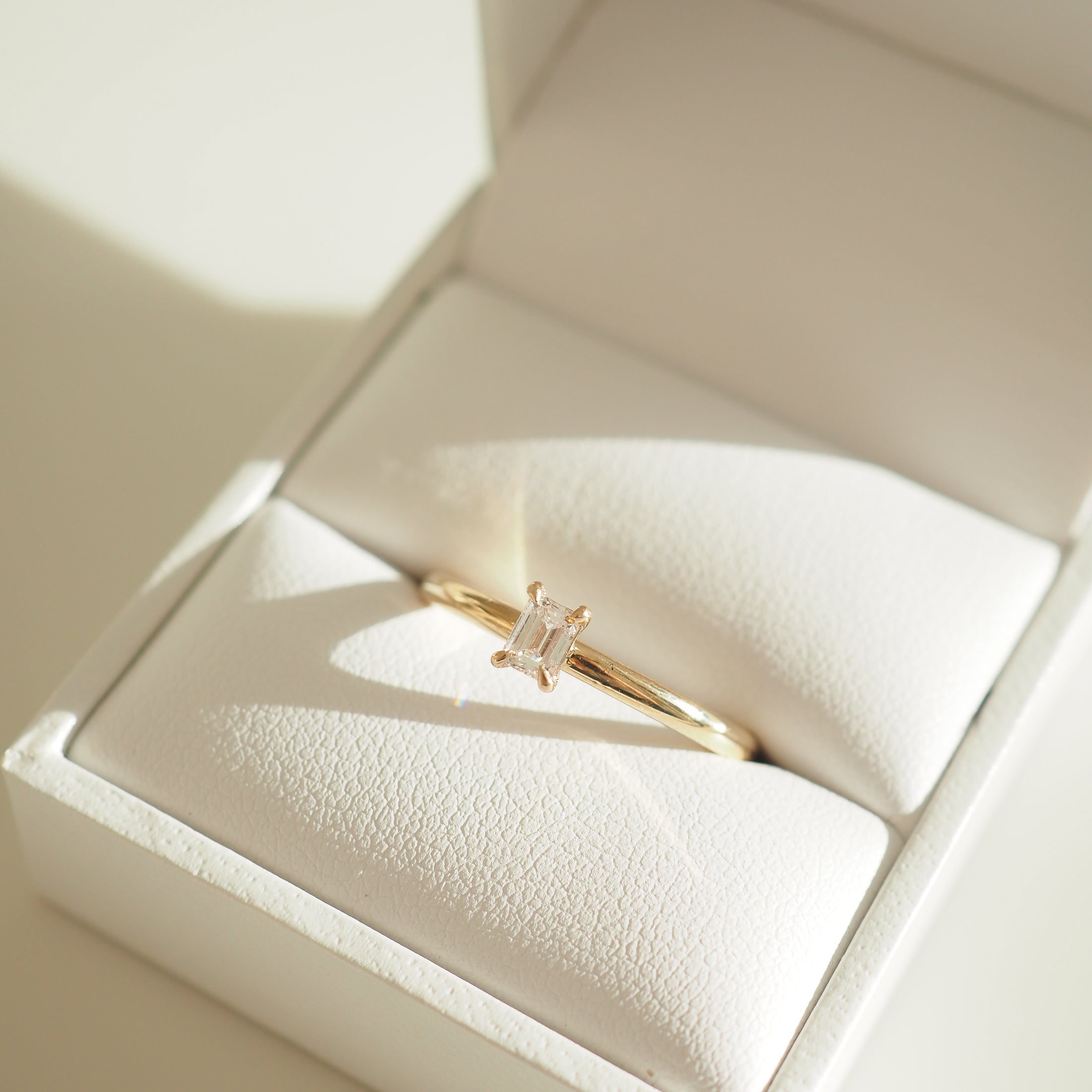 Elegant gold ring with a rectangular diamond in a white jewellery box, showcasing luxury and refined craftsmanship.