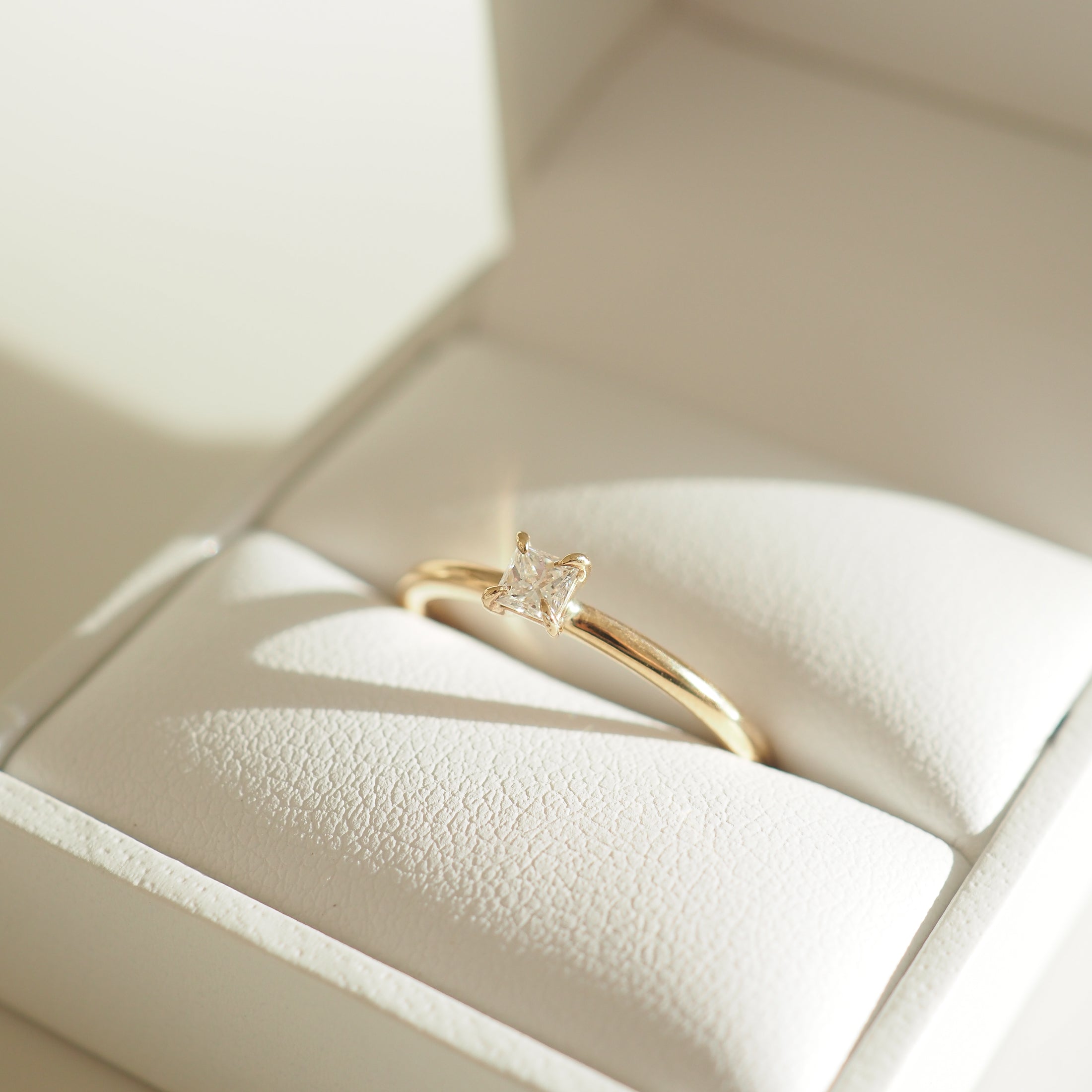 Gold ring with a square diamond set against a white leather jewellery box, capturing luxurious elegance.