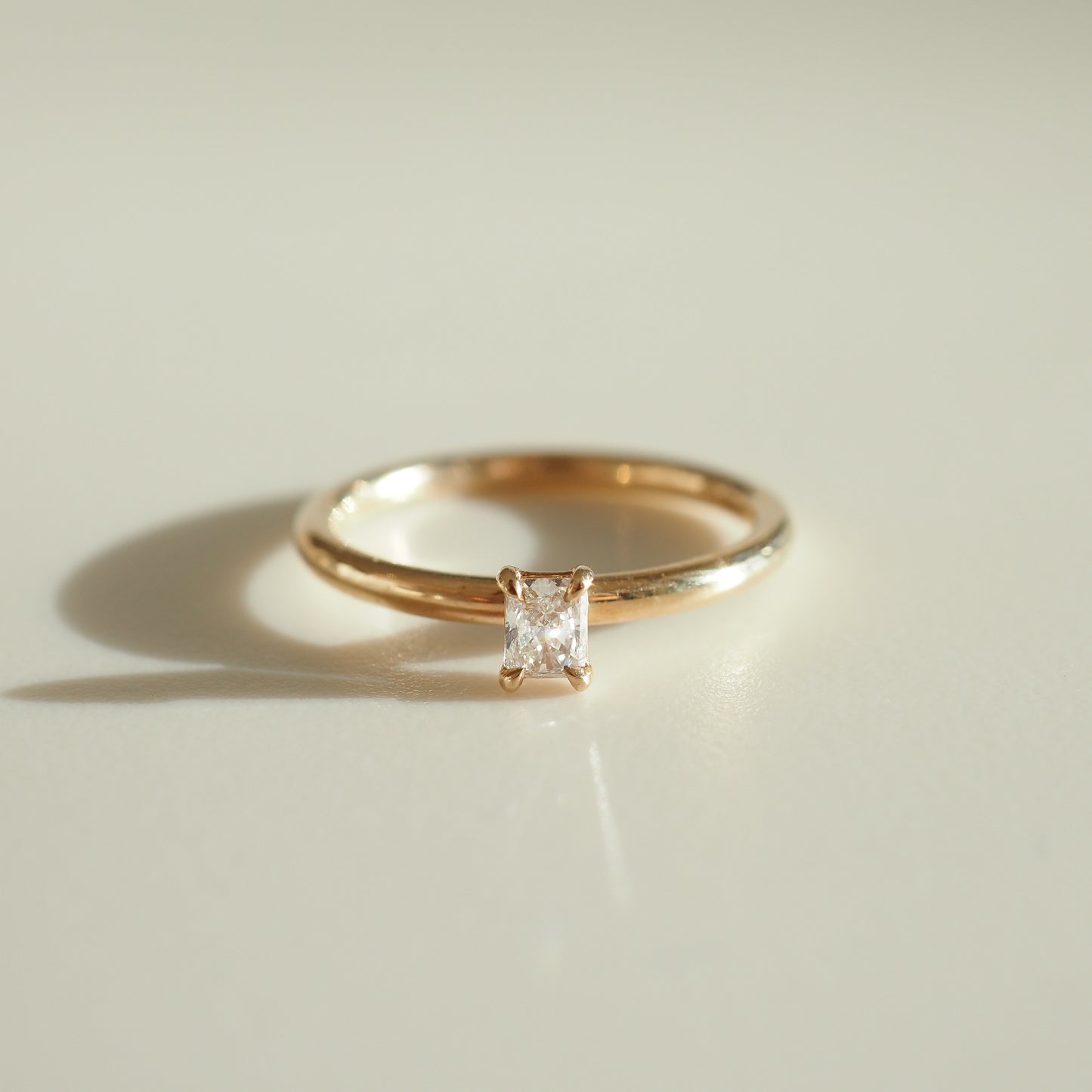 A delicate gold ring with a single princess-cut diamond, bathed in soft sunlight, symbolising luxury and elegance in fine jewellery.