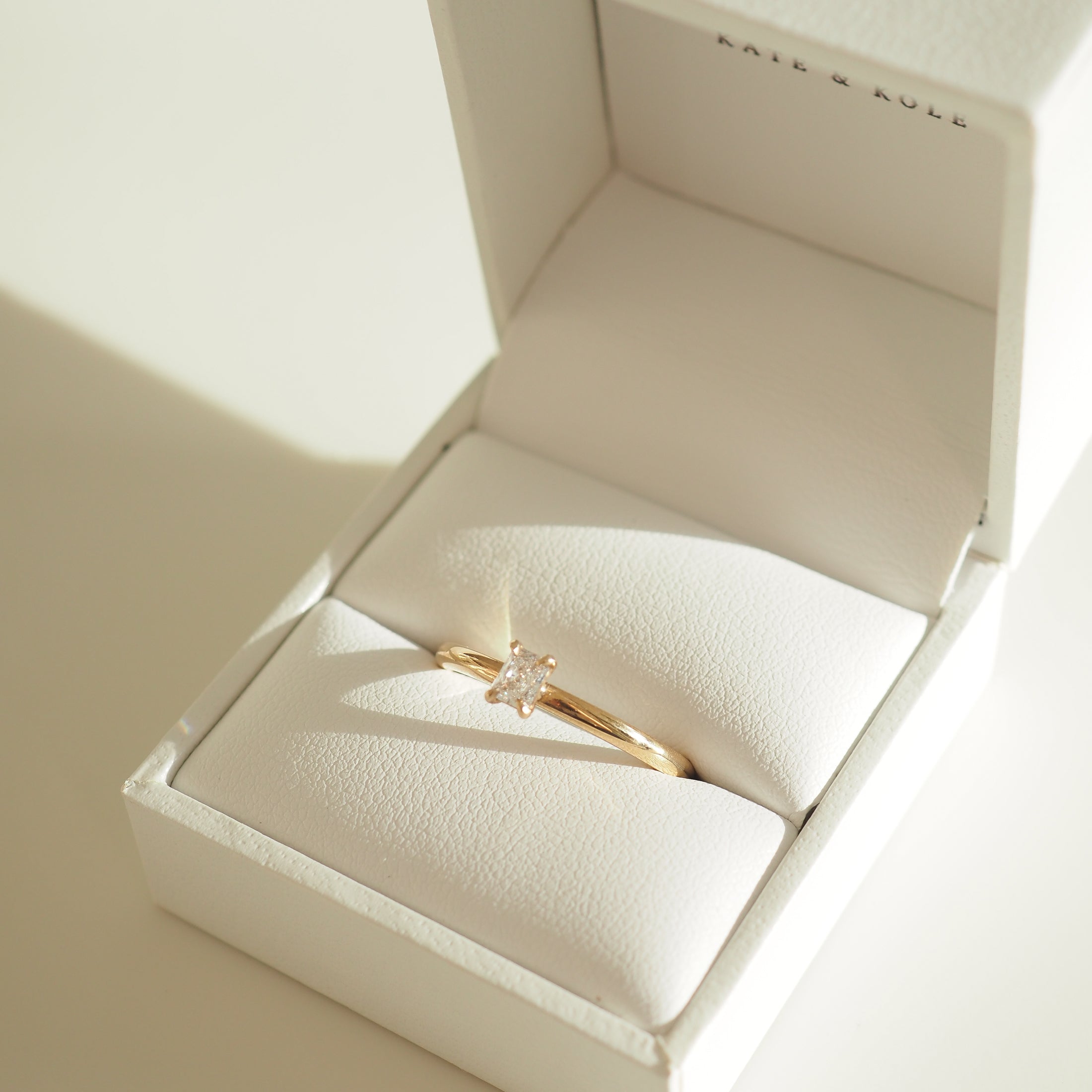 Gold engagement ring with a square-cut diamond, elegantly displayed in a white jewellery box. Luxurious and sophisticated design.