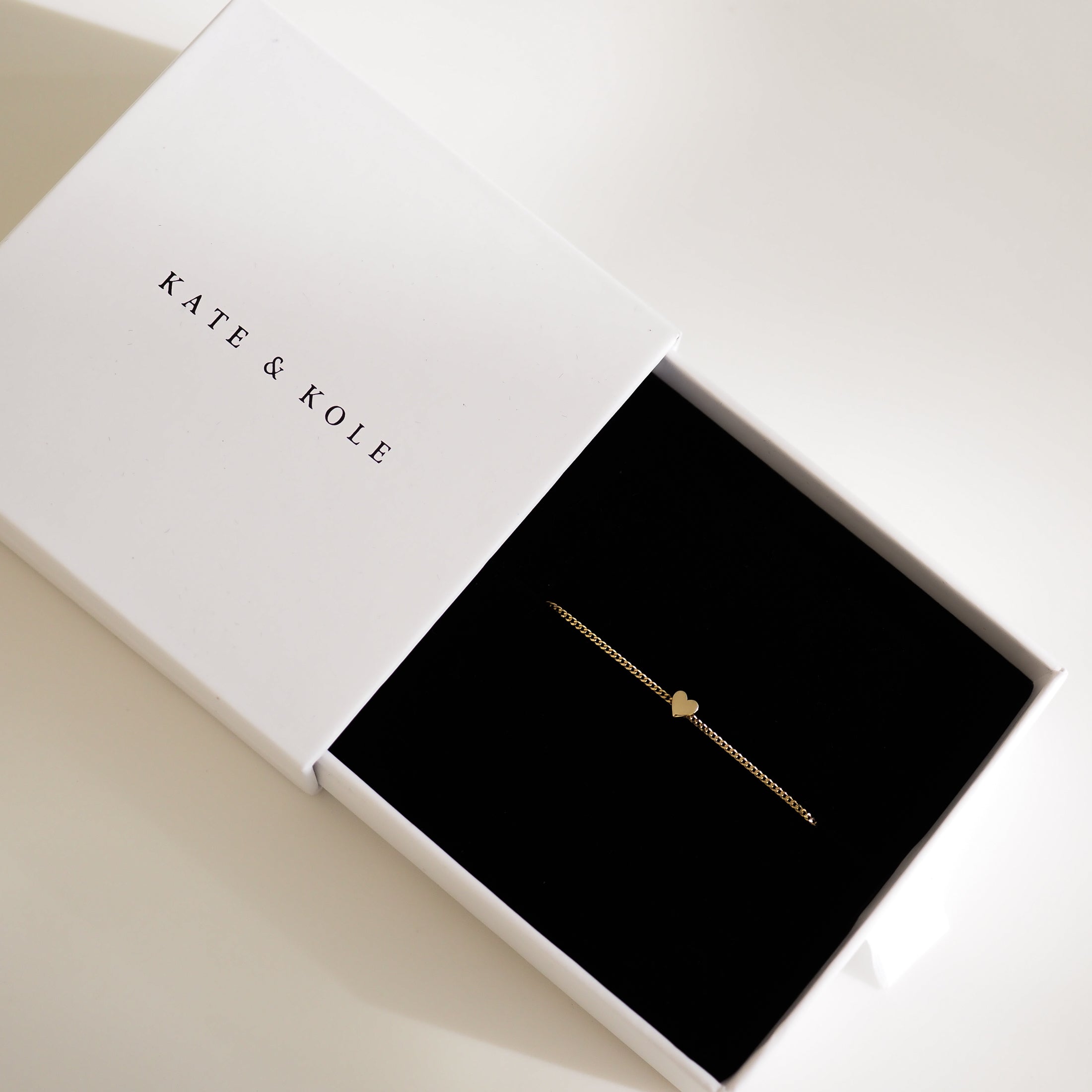 Gold heart bracelet displayed in an elegant Kate & Kole jewellery box, contrasting against the sleek black interior.