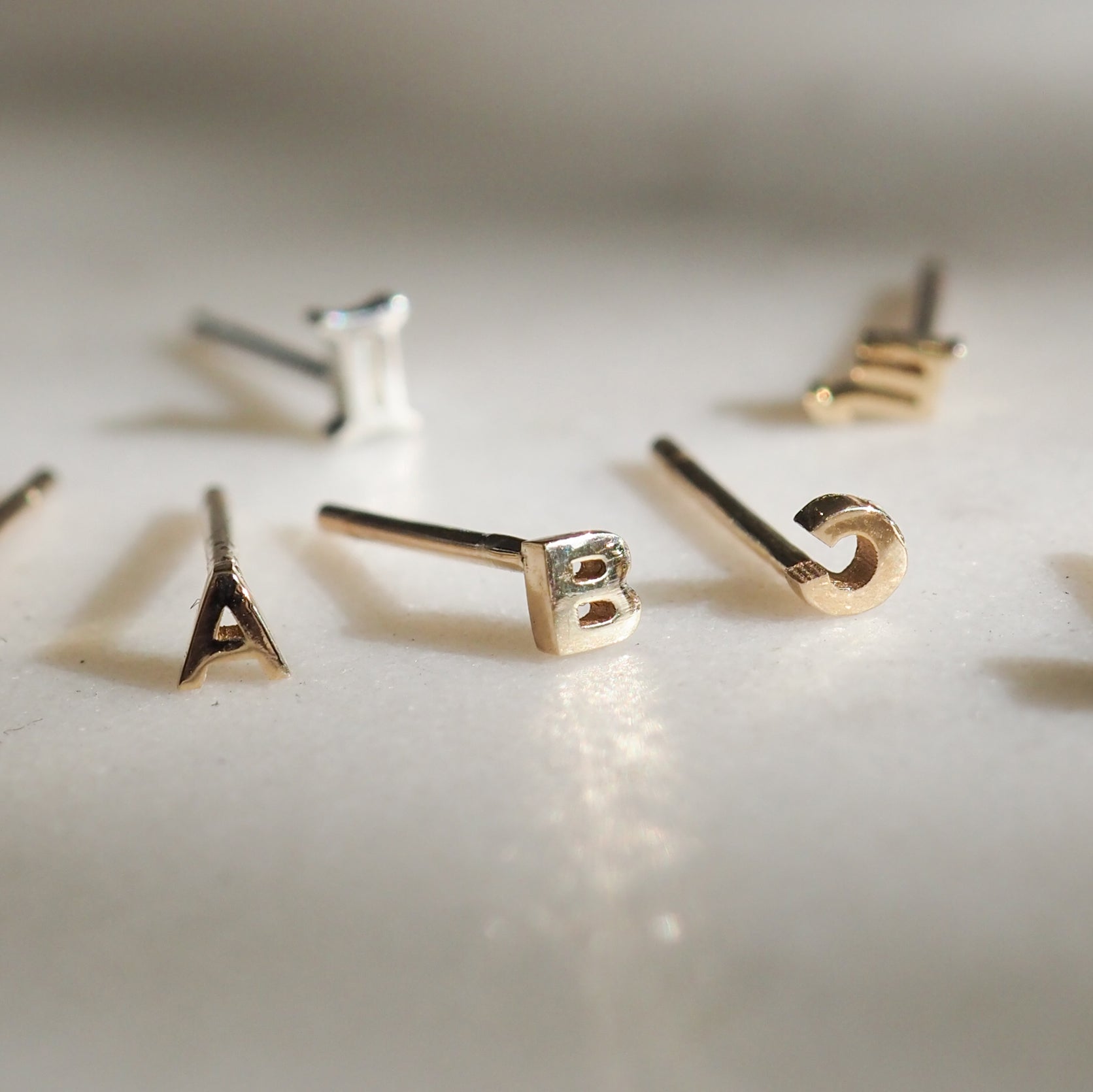 Close-up of luxury gold and silver alphabet earrings, featuring letters A to E, elegantly displayed on a white surface.